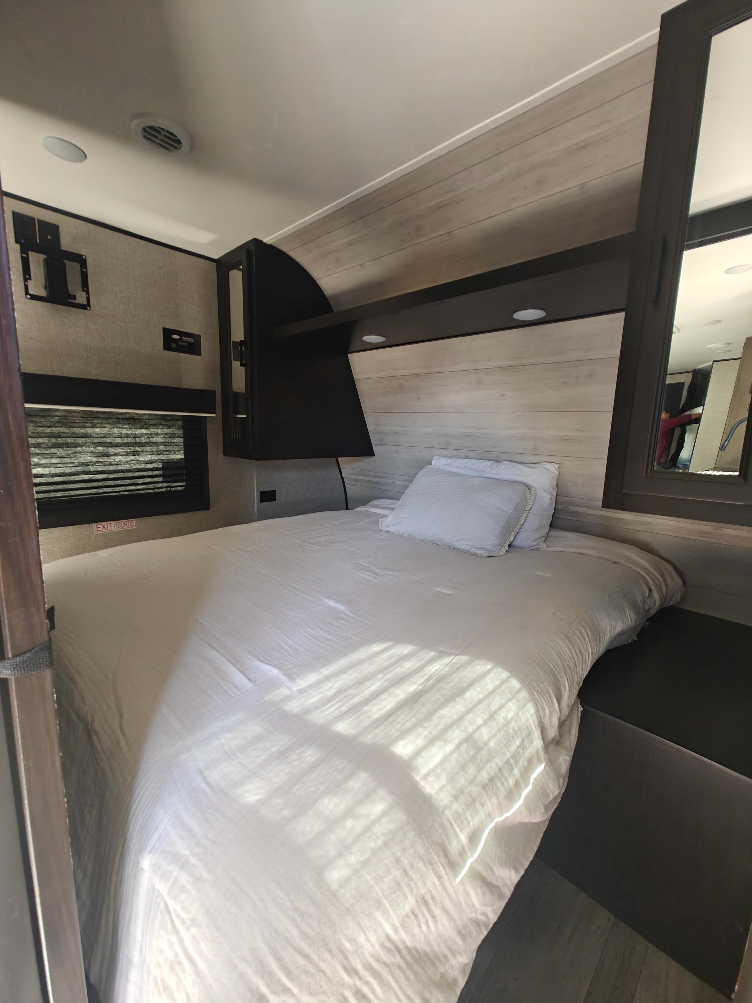 Bright RV rental bedroom with white bed, light wood-look walls, a TV mount, an exit window, and a storage cabinet.. Jayco Jay Flight SLX Rocky Mountain Edition 2022