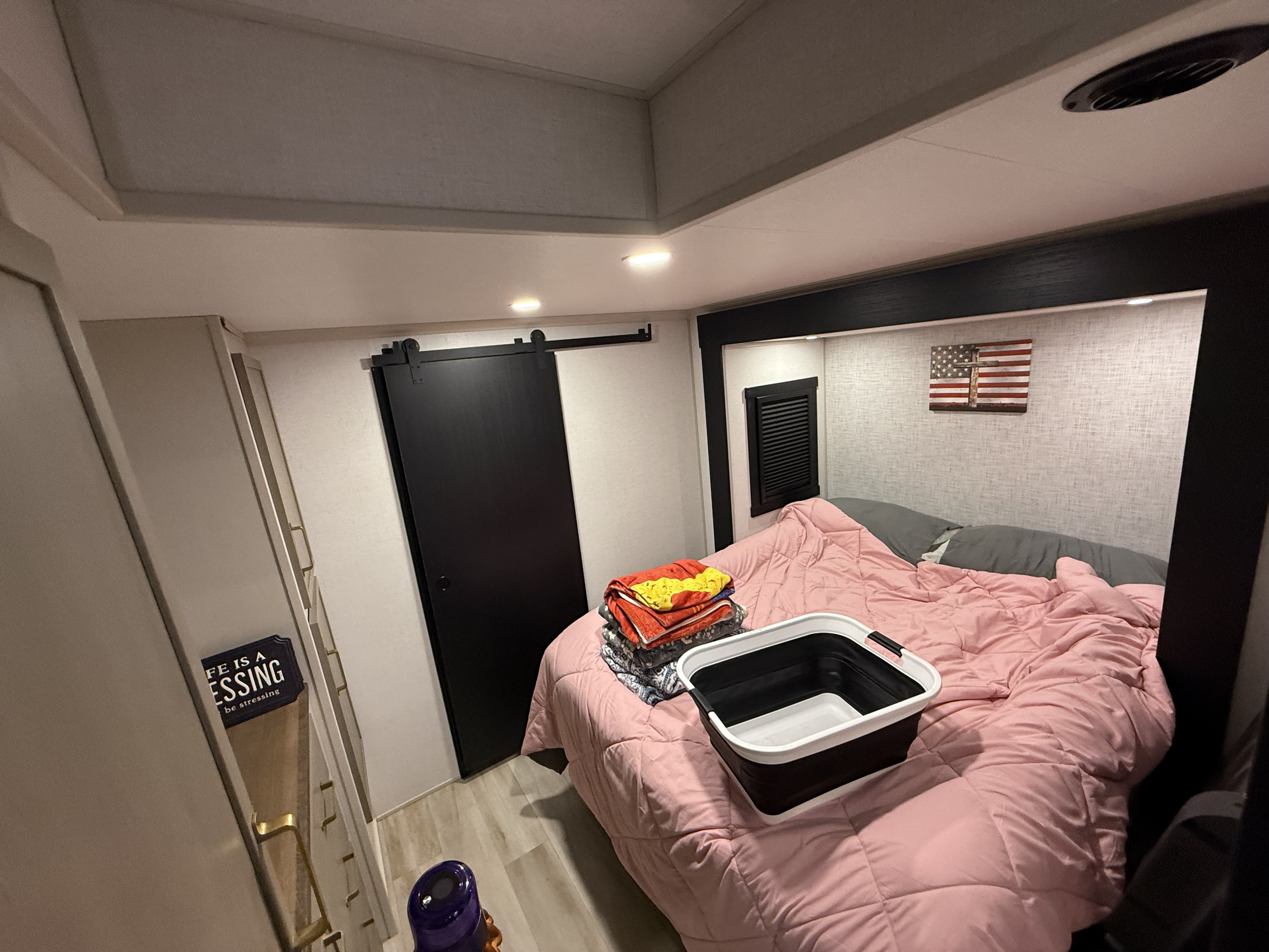 Cozy RV rental bedroom: bed with pink comforter, black barn door, built-in storage, American flag art, laundry basket.. Forest River Salem Hemisphere 2025