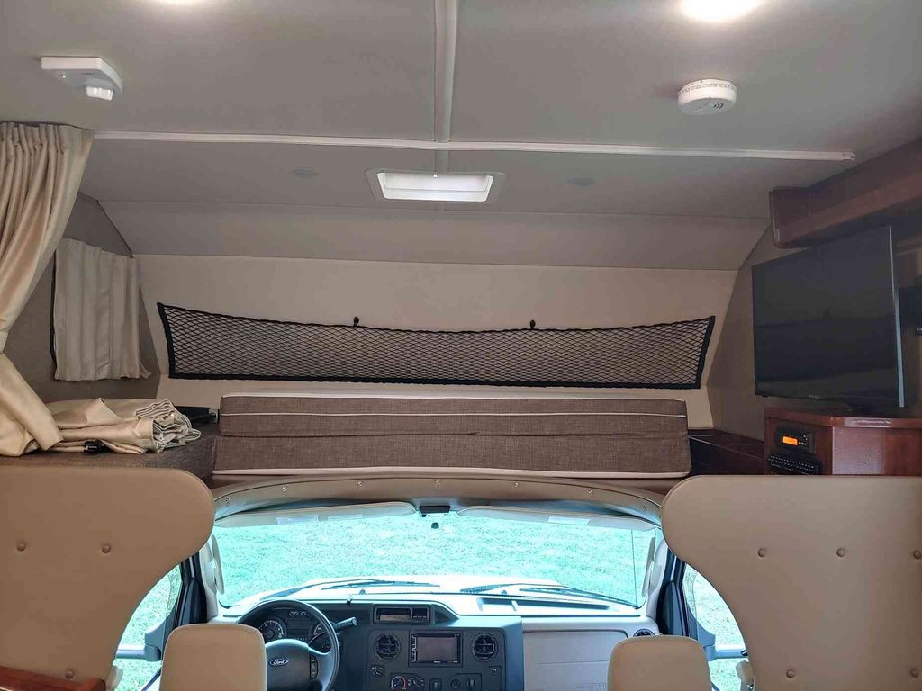 **RV rental** interior: Front view showing cab-over bunk with safety net, cockpit, TV, and ceiling safety detector.. Holiday Rambler Altera 2018