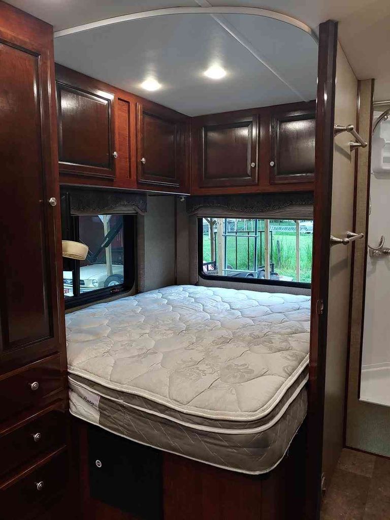 RV rental bedroom: a cozy interior with a quilted bed, dark wooden cabinets overhead, and windows on each side.. Holiday Rambler Altera 2018