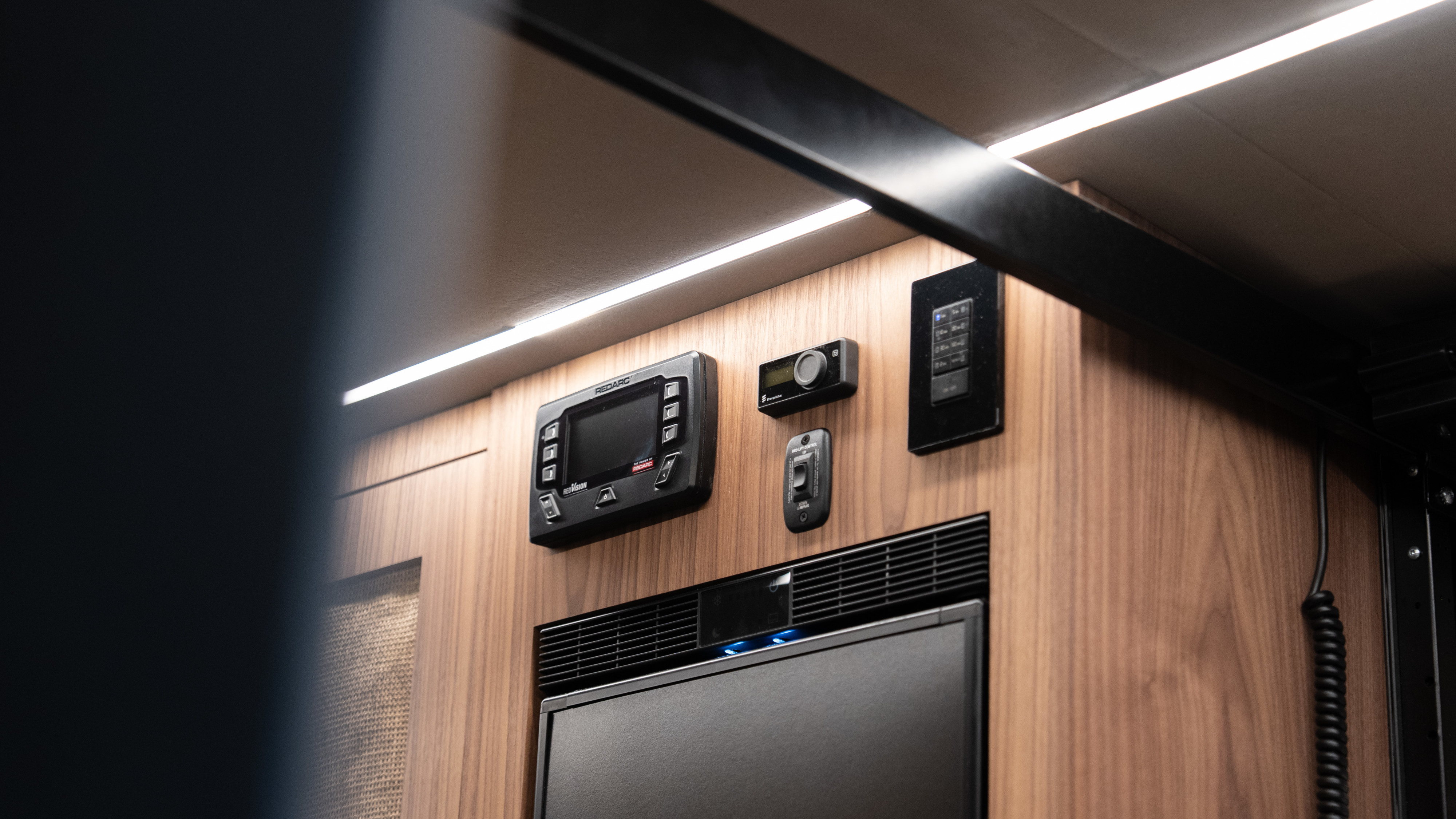 RV rental's interior features modern controls: Redarc RedVision power display, bed lift switch, and LED accent lighting.. Other Sandy Vans 2025