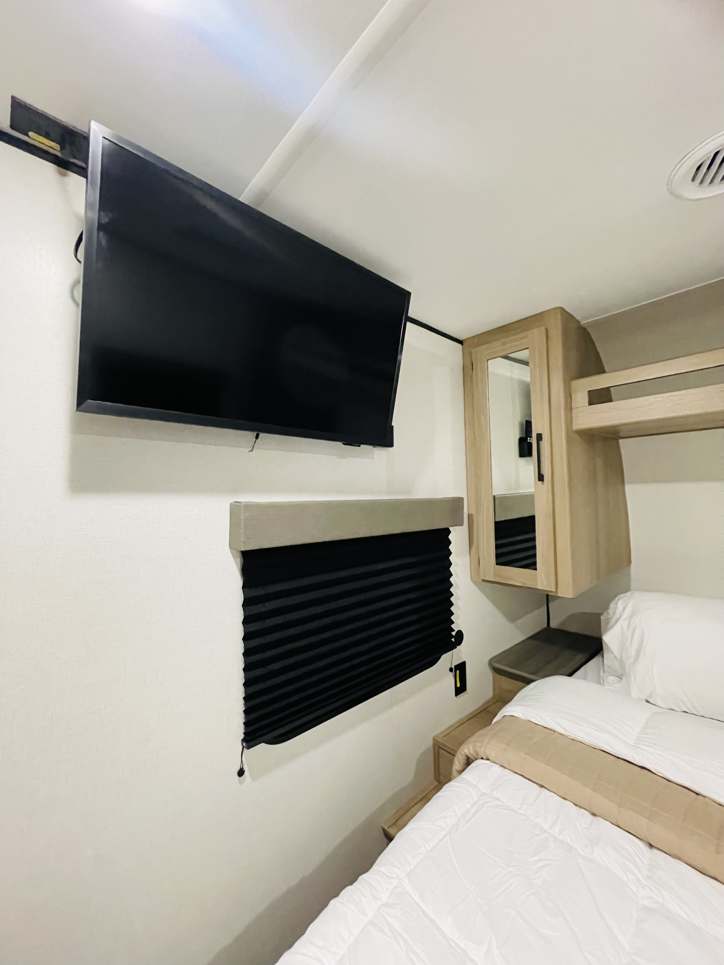 Cozy RV rental bedroom featuring a wall-mounted TV, black pleated blind, wood storage cabinet, and a comfortable bed.. Keystone Coleman LANTERN 32BHS 2026