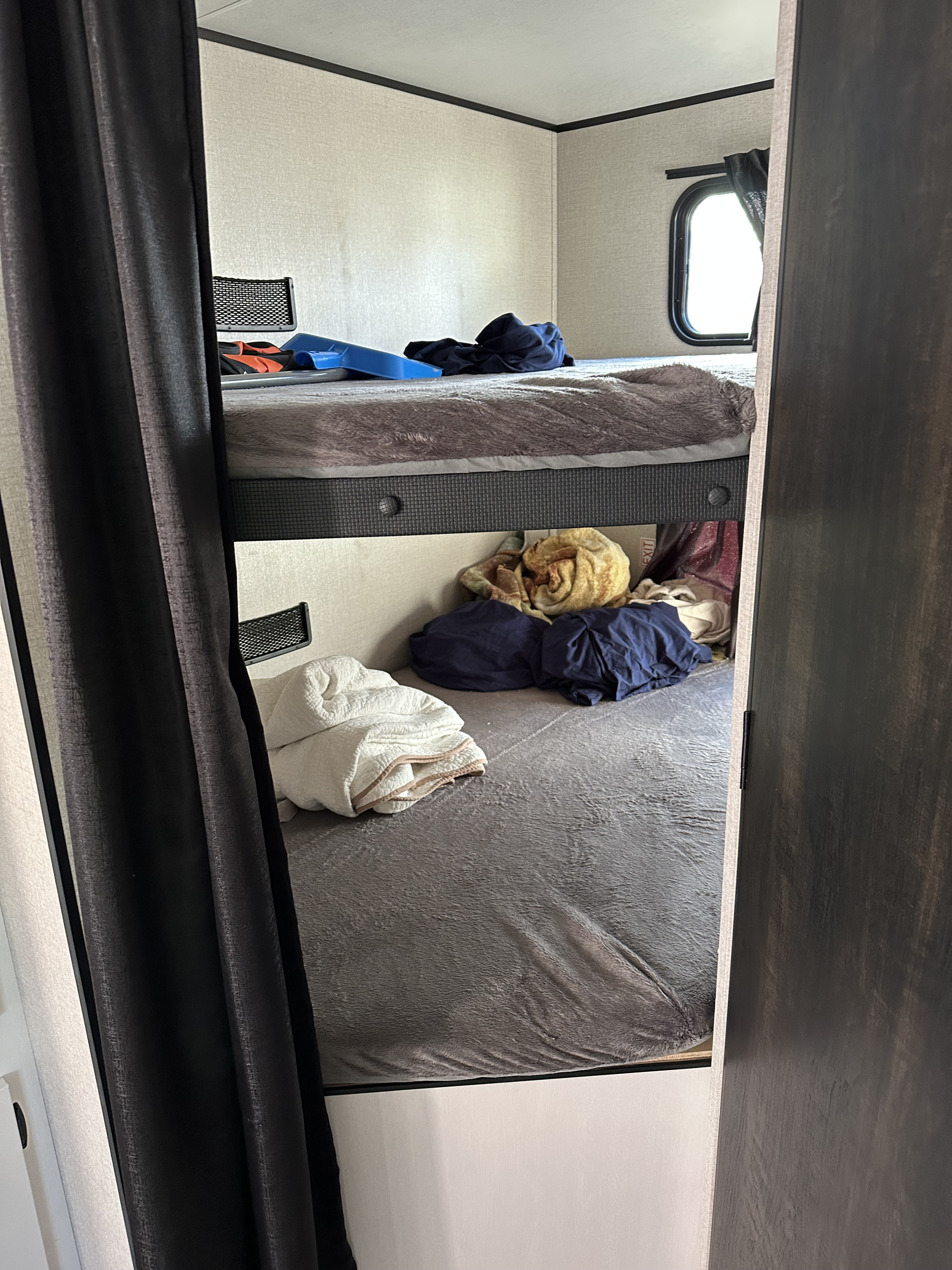 A clear view inside an **rv rental**, featuring a two-tier bunk bed. Blankets and belongings are on both beds; a small window is seen.. Wayfinder RV GoPlay 26BHS 2024