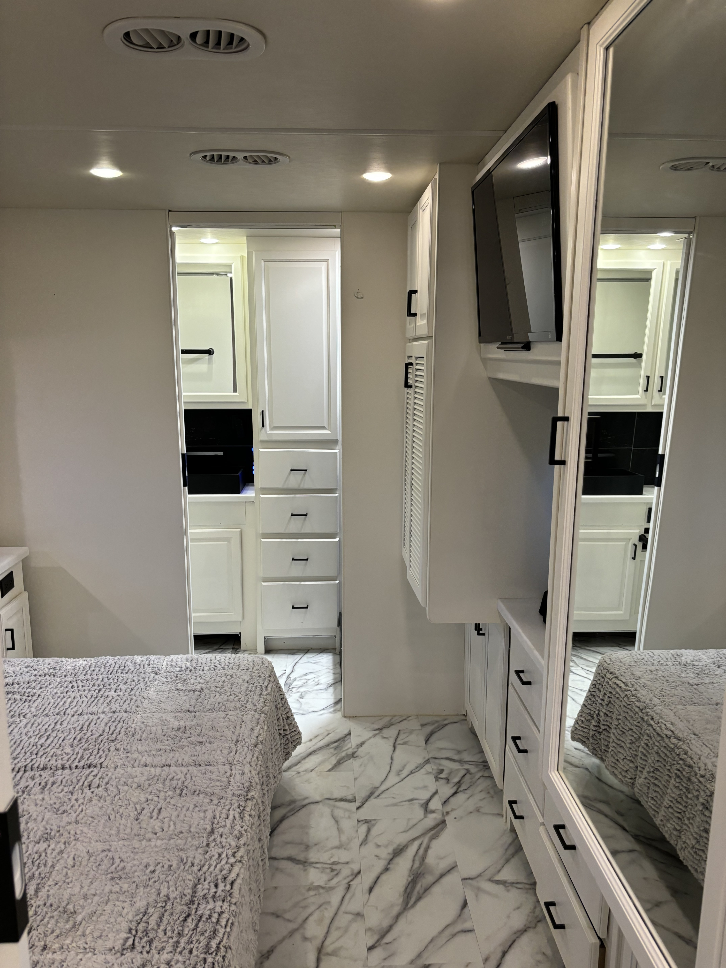 Experience this modern RV rental bedroom featuring white cabinets, a cozy bed, marble-look floor, and mounted TV.. Fleetwood Bounder 2016