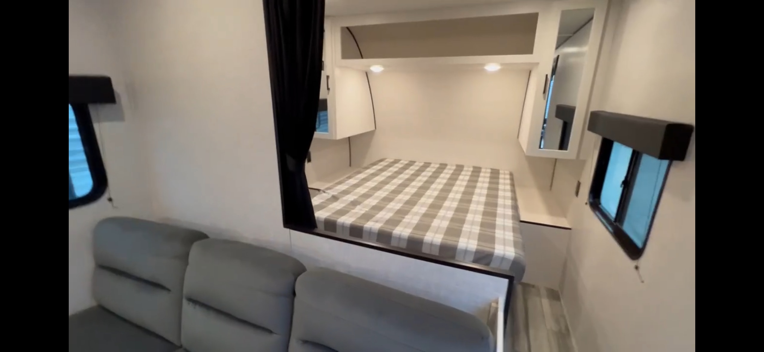 Cozy rv rental interior: Queen bed with plaid bedding, overhead cabinets, a sofa, and windows create a compact living space.. Jayco Jay Flight SLX 2025