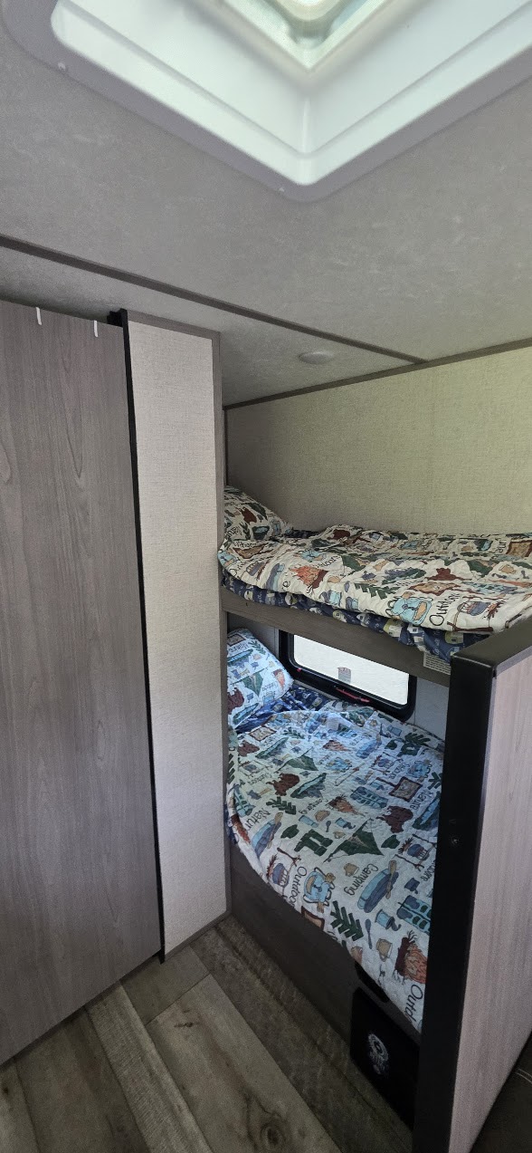 RV rental interior featuring cozy bunk beds with colorful bedding. The lower bunk has a window, and a closet is on the left.. Dutchmen Coleman Lantern LT 2023