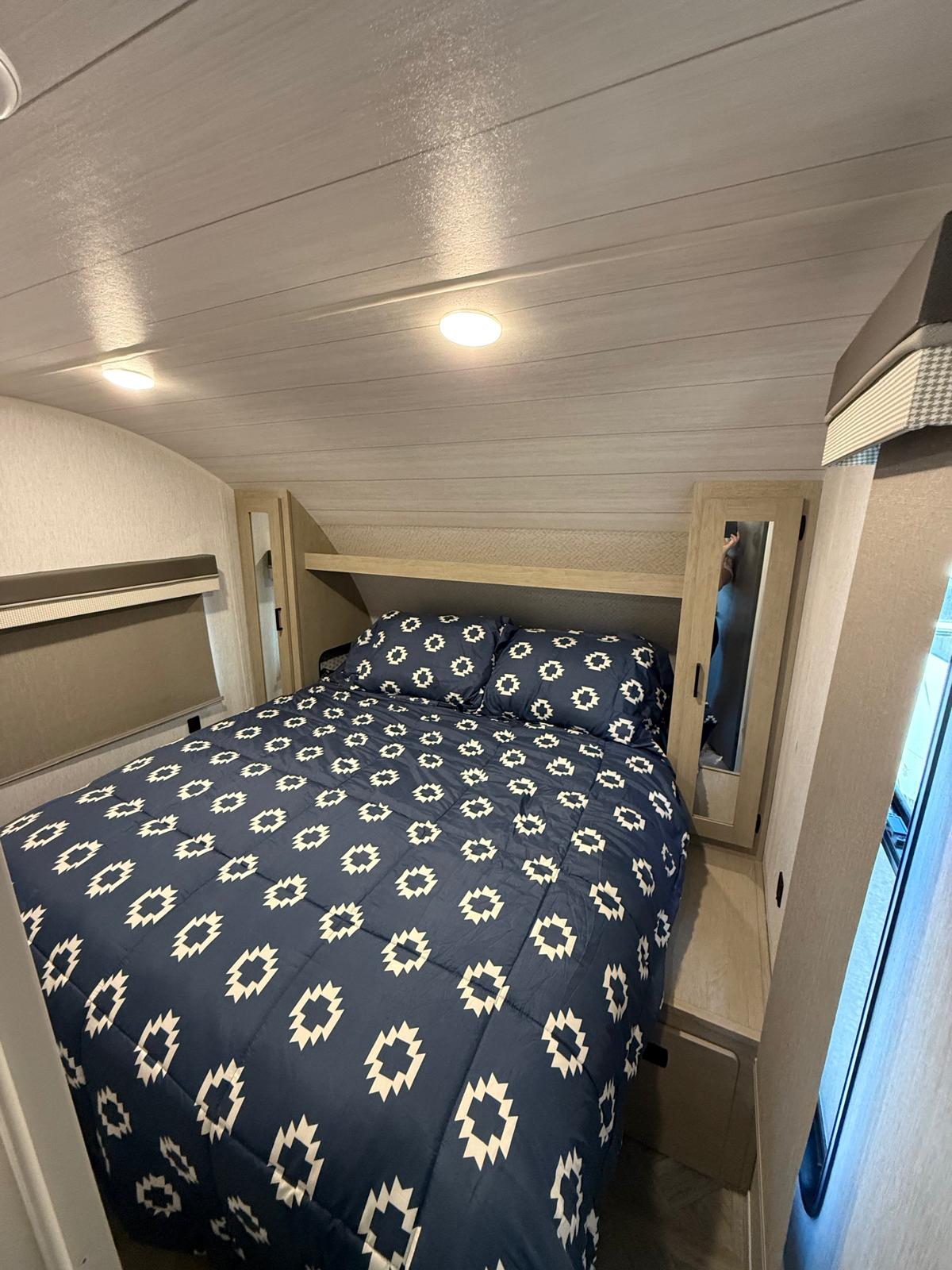 RV rental bedroom: a cozy space featuring a navy geometric bed, wood-look ceiling, bright overhead lights, and built-in mirrored storage.. Forest River Salem Cruise Lite Platinum 2023