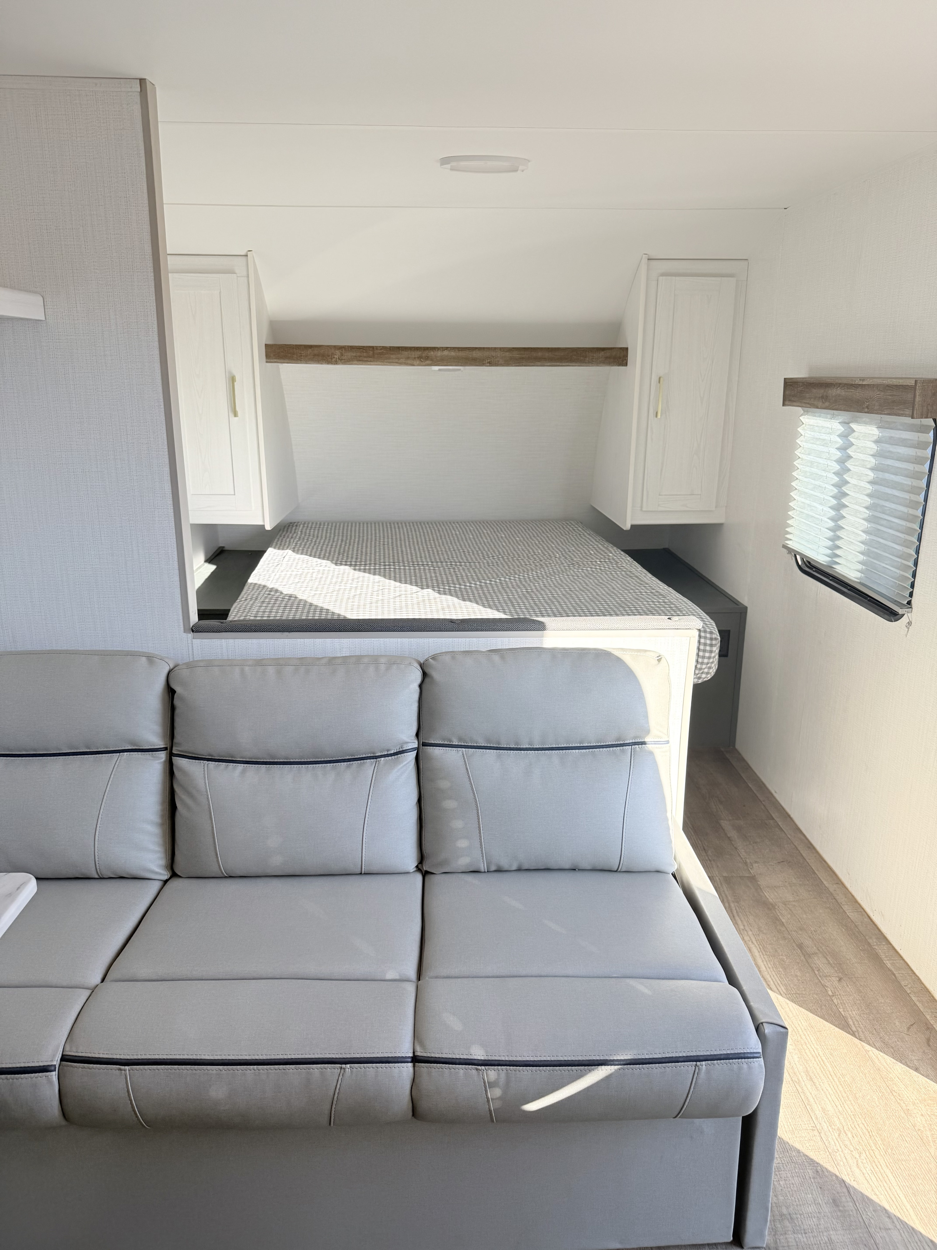 Clean & bright RV rental interior with a light gray sofa and a cozy bed area, showcasing modern design for comfortable travel.. Heartland recreational vehicles 251BH-c 2024