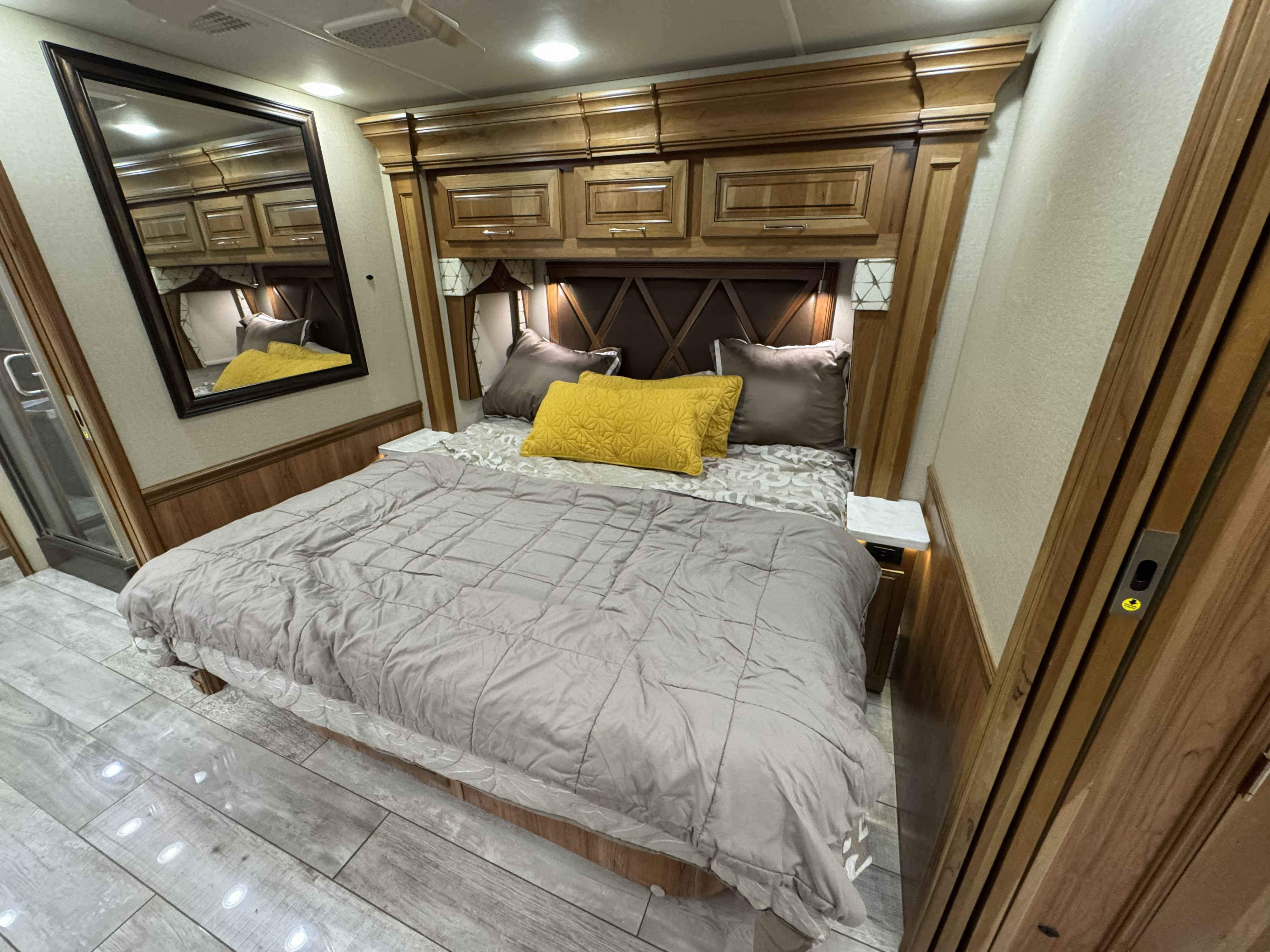Cozy RV rental bedroom with a large bed, golden pillows, wooden storage, and a full-length mirror. Perfect travel space.. Entegra Coach Anthem 2019