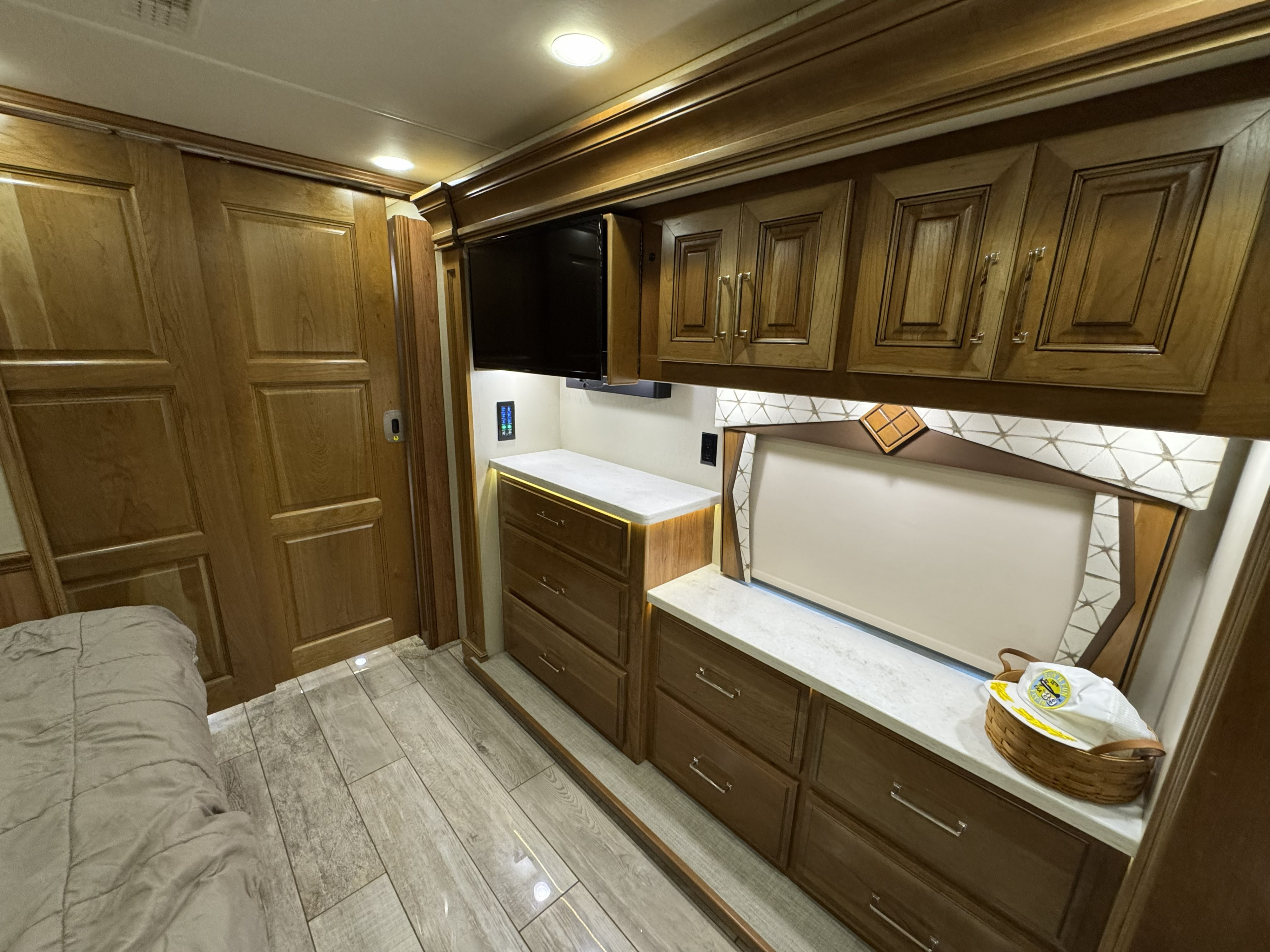 Inside a luxurious RV rental bedroom with warm wood cabinetry, a TV, and under-cabinet lighting for comfort and style.. Entegra Coach Anthem 2019