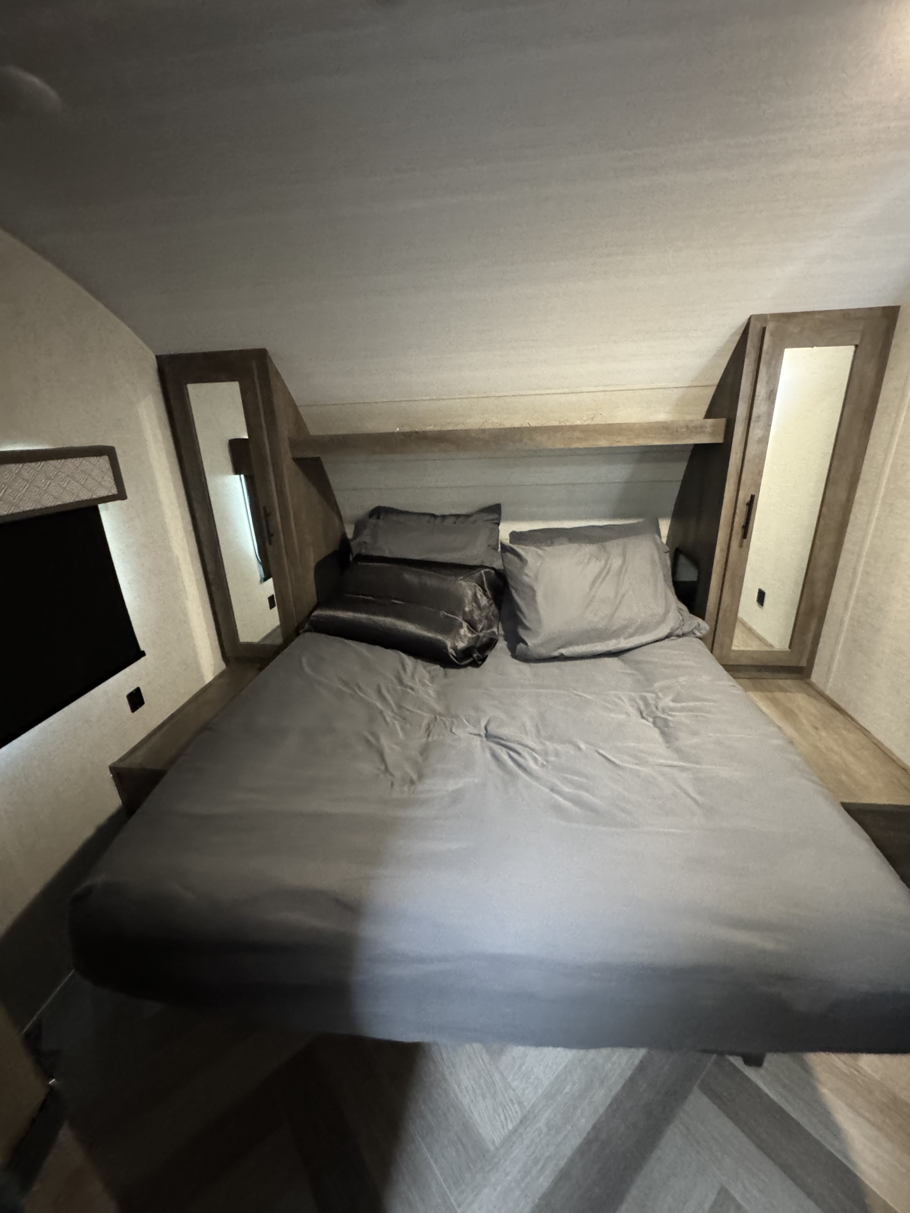 RV rental bedroom with a grey bed, shelf headboard, and mirrored wardrobes, offering cozy and compact living.. Forest River Wildwood X-Lite 2021