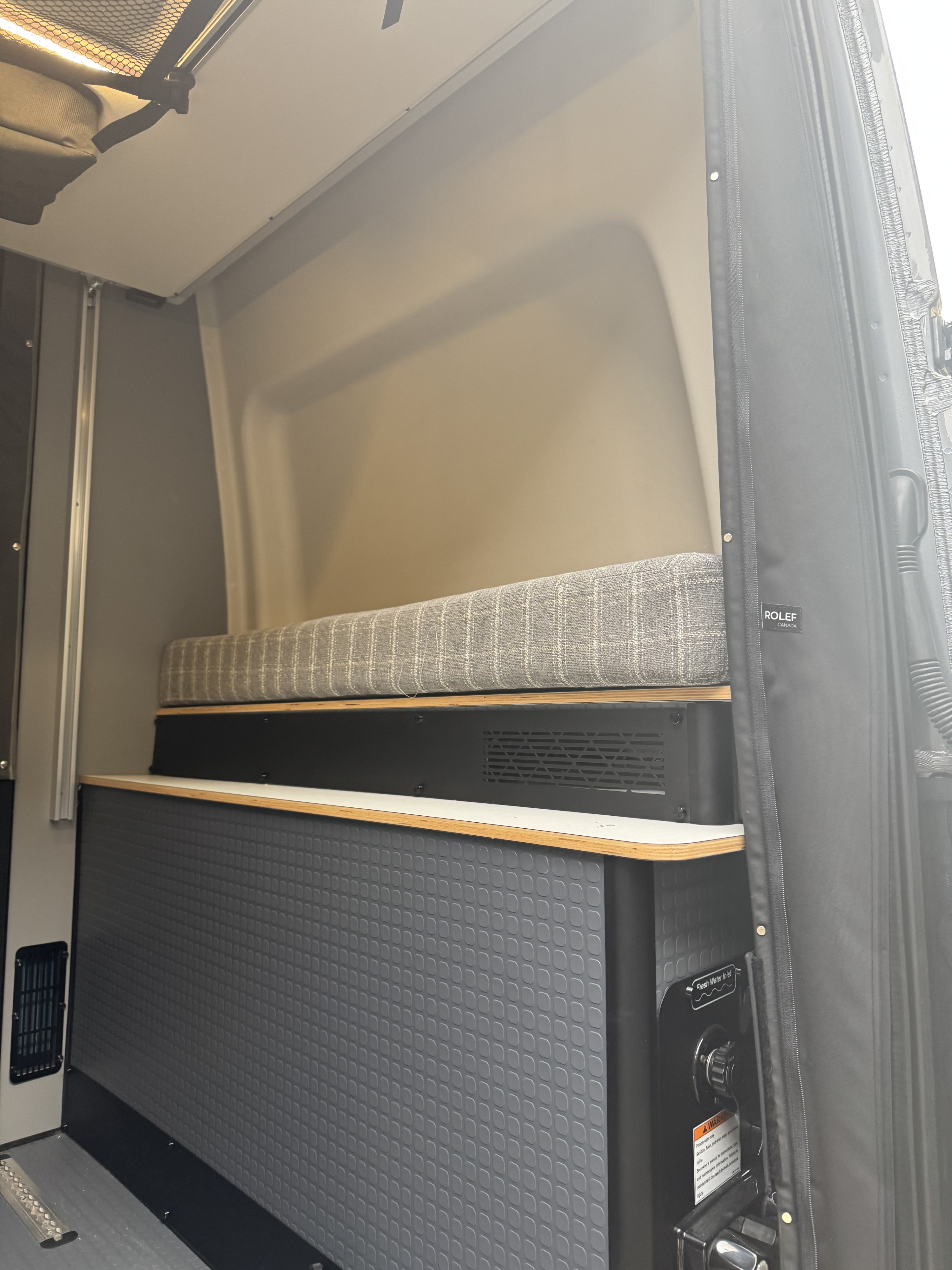 RV rental interior featuring a cushioned bench, lower textured cabinetry, and a fresh water inlet.. Winnebago Revel 2025