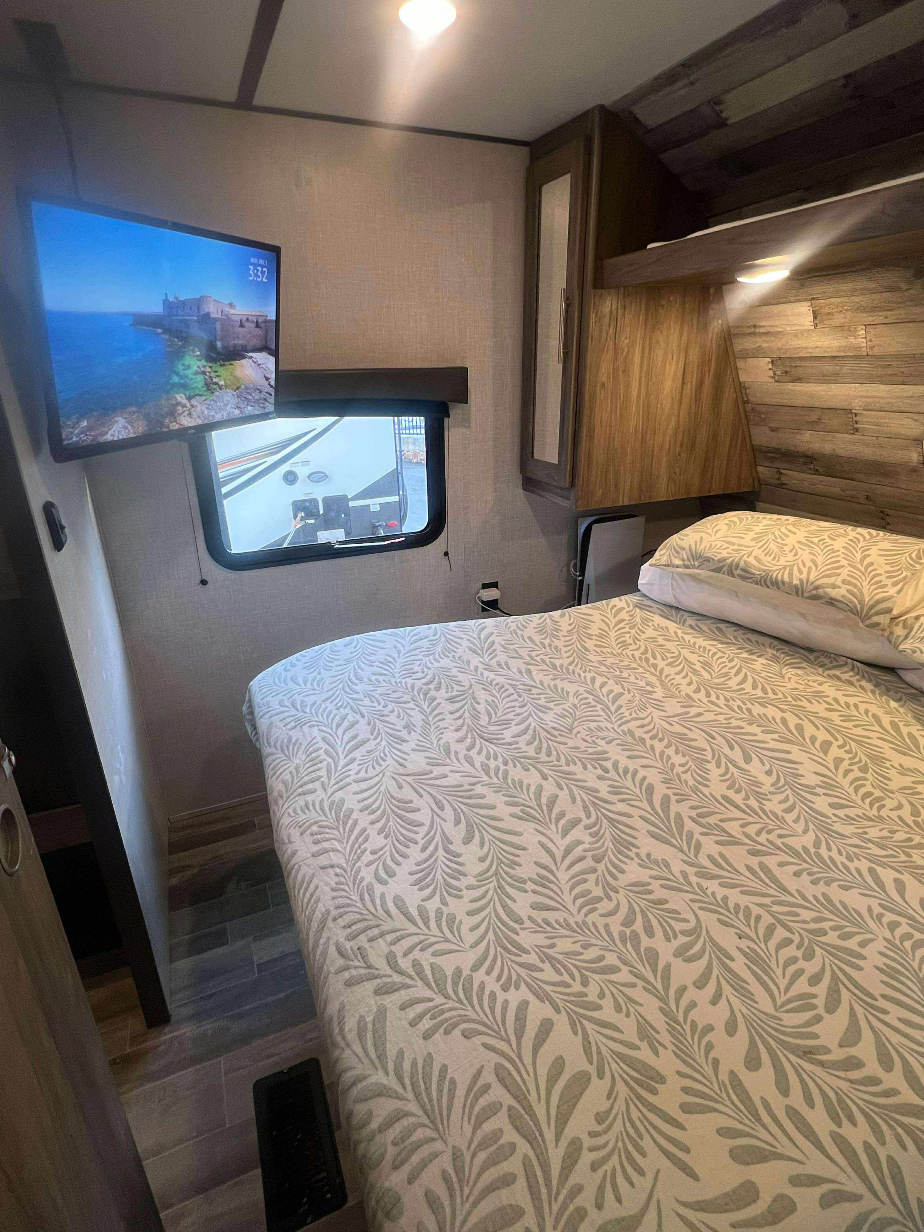 A comfortable RV rental bedroom featuring a large bed with patterned linens, a wall-mounted TV, and built-in storage.. Heartland RVs Pioneer 2018