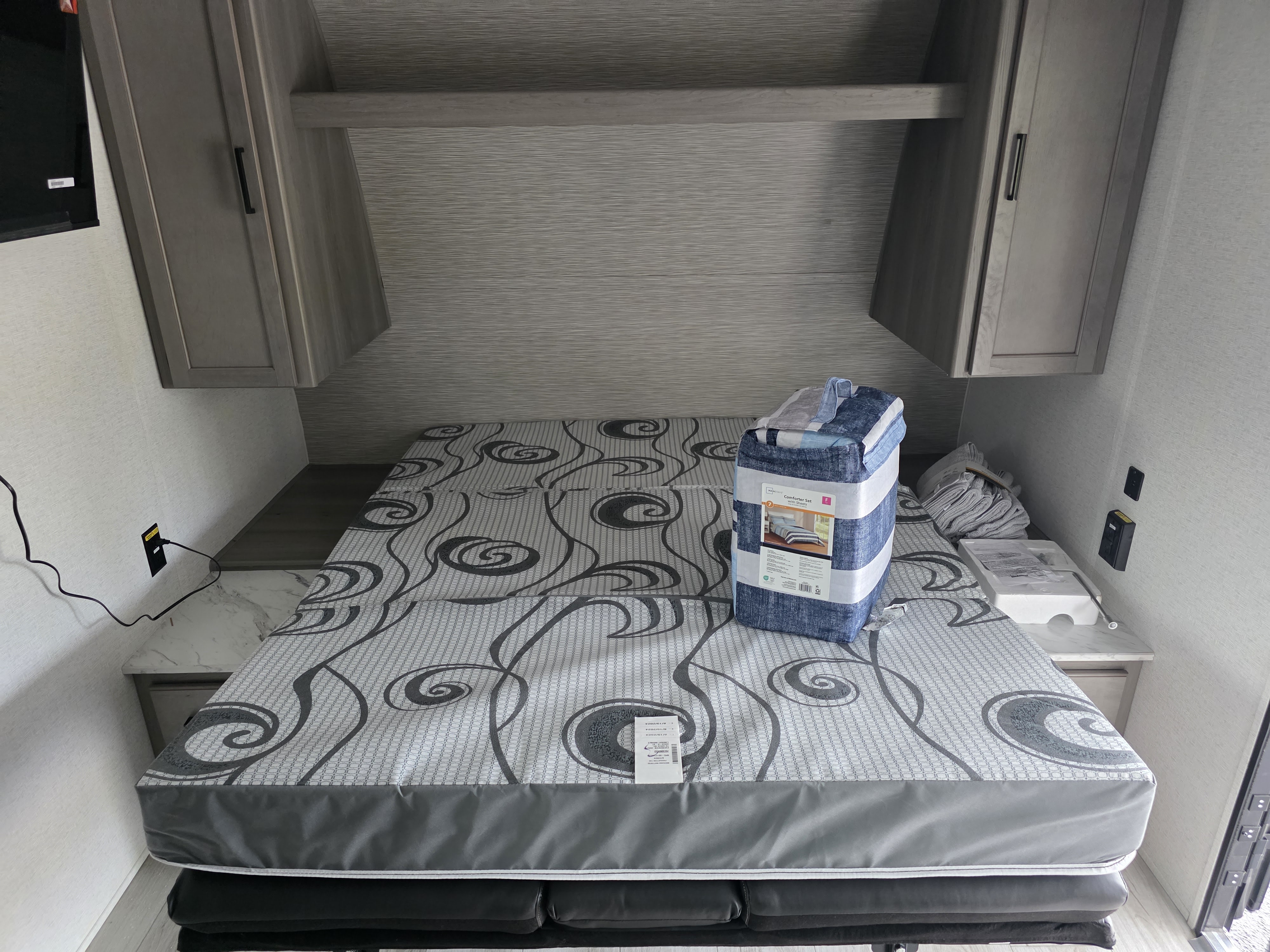 Inside an rv rental: a cozy sleeping area featuring a patterned mattress, new bedding set, and convenient overhead cabinets.. Keystone RV Hideout 2025