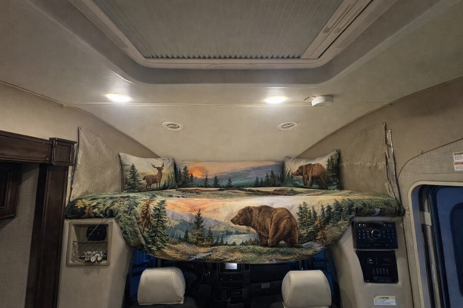 RV rental: Overhead cab-over bed with wilderness-themed bedding, showcasing bears, deer, and a forest scene.. Thor Synergy 2017