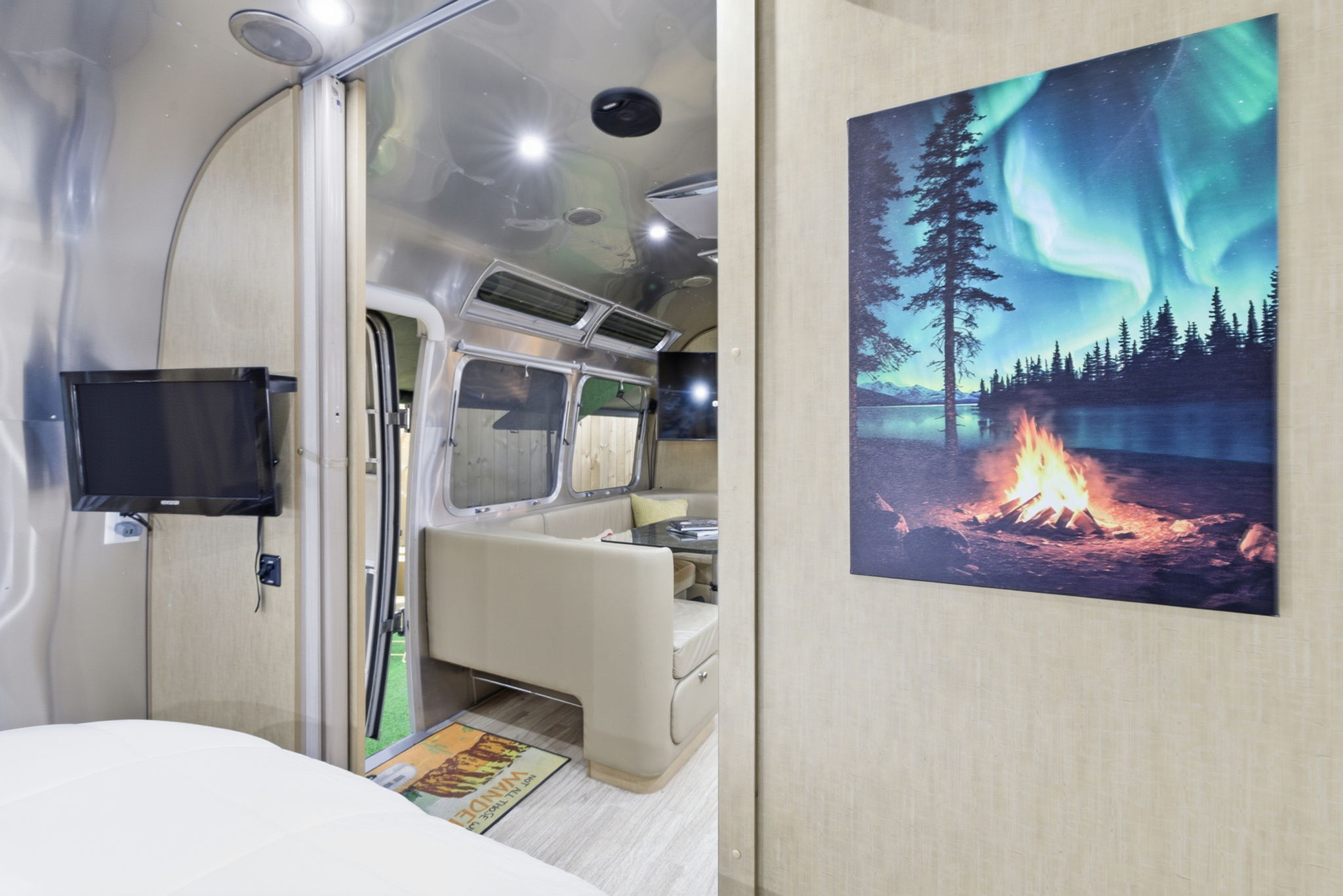 Inside a stylish RV rental: a comfortable bed, TV, and dining booth. A vibrant art print of an aurora and campfire adorns the wall.. Airstream Flying Cloud 2015