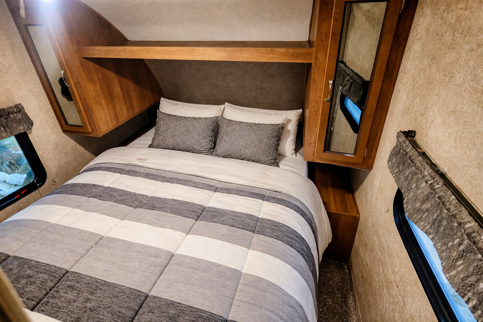 This cozy RV rental bedroom features a striped bed, pillows, wooden cabinetry, and windows with blinds, ideal for travel.. Coachmen Coachmen Catalina SBX 261BHS 2019