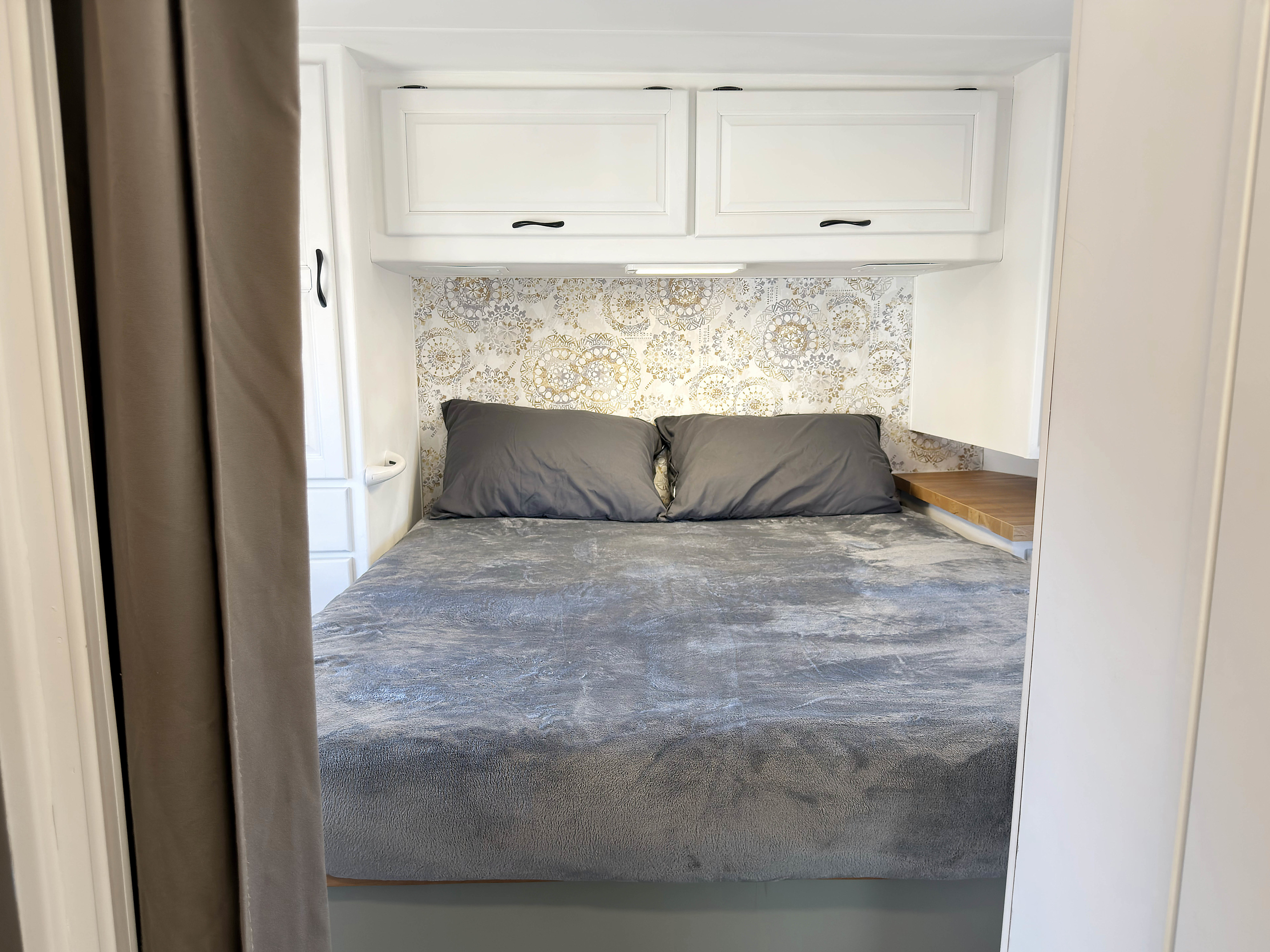 Cozy RV rental bedroom with patterned wallpaper, overhead cabinets, and a comfy grey bed.. Thor Majestic 2012
