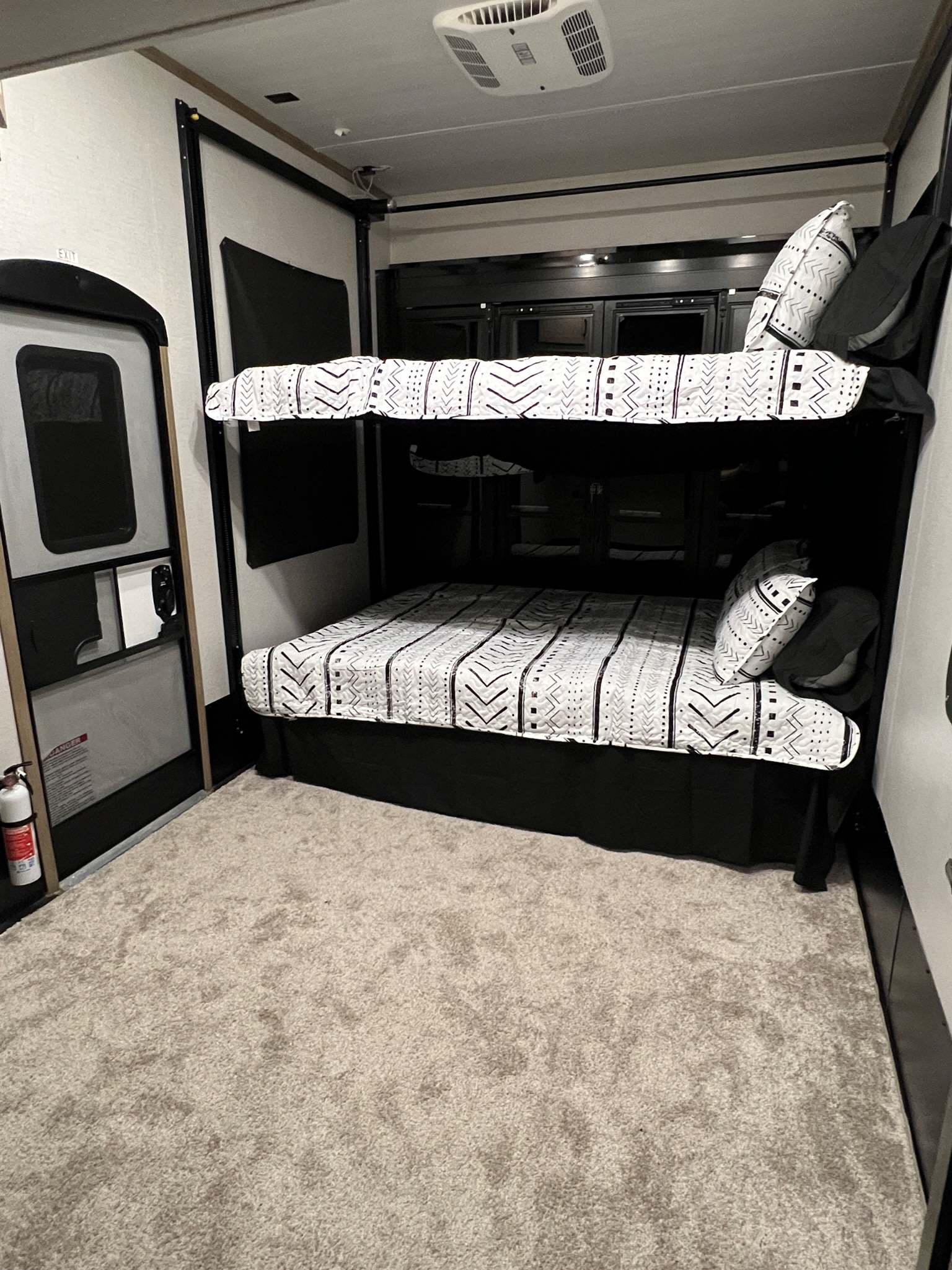This RV rental interior features sleek bunk beds with patterned bedding, an RV door, and ceiling AC for comfortable sleeping.. Keystone Raptor 2022