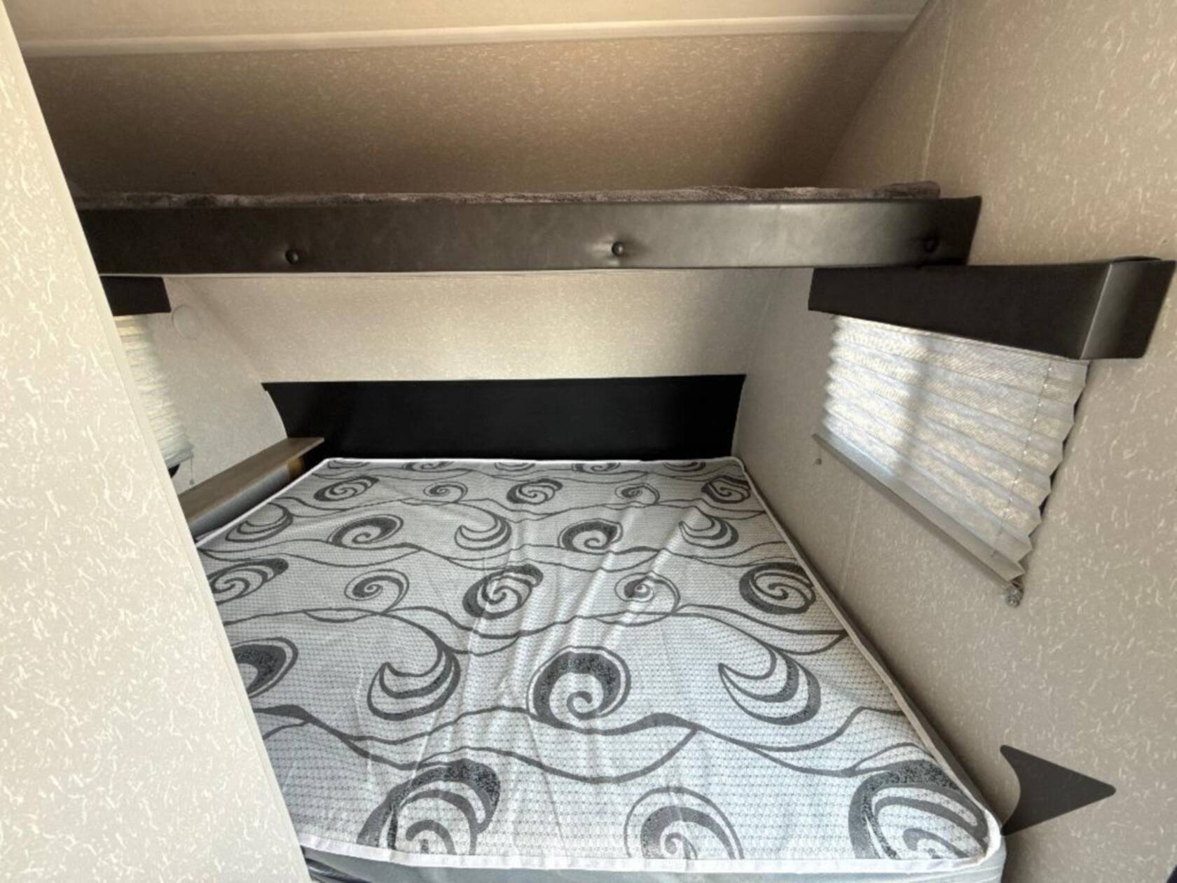 Cozy RV rental sleeping area with a lower bed, upper bunk bed, and window with pleated blind.. Forest River Cherokee Wolf Pup 2022