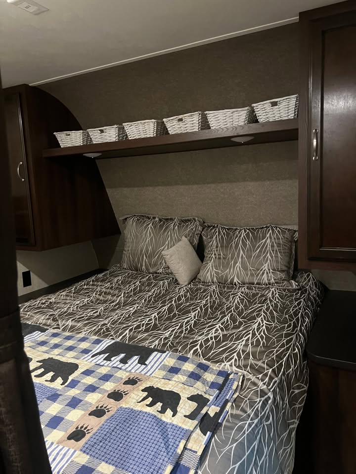 Cozy RV rental bedroom with tree-patterned bedding, a bear quilt, overhead storage baskets, and dark wood cabinetry.. Jayco Jay Flight SLX 2018