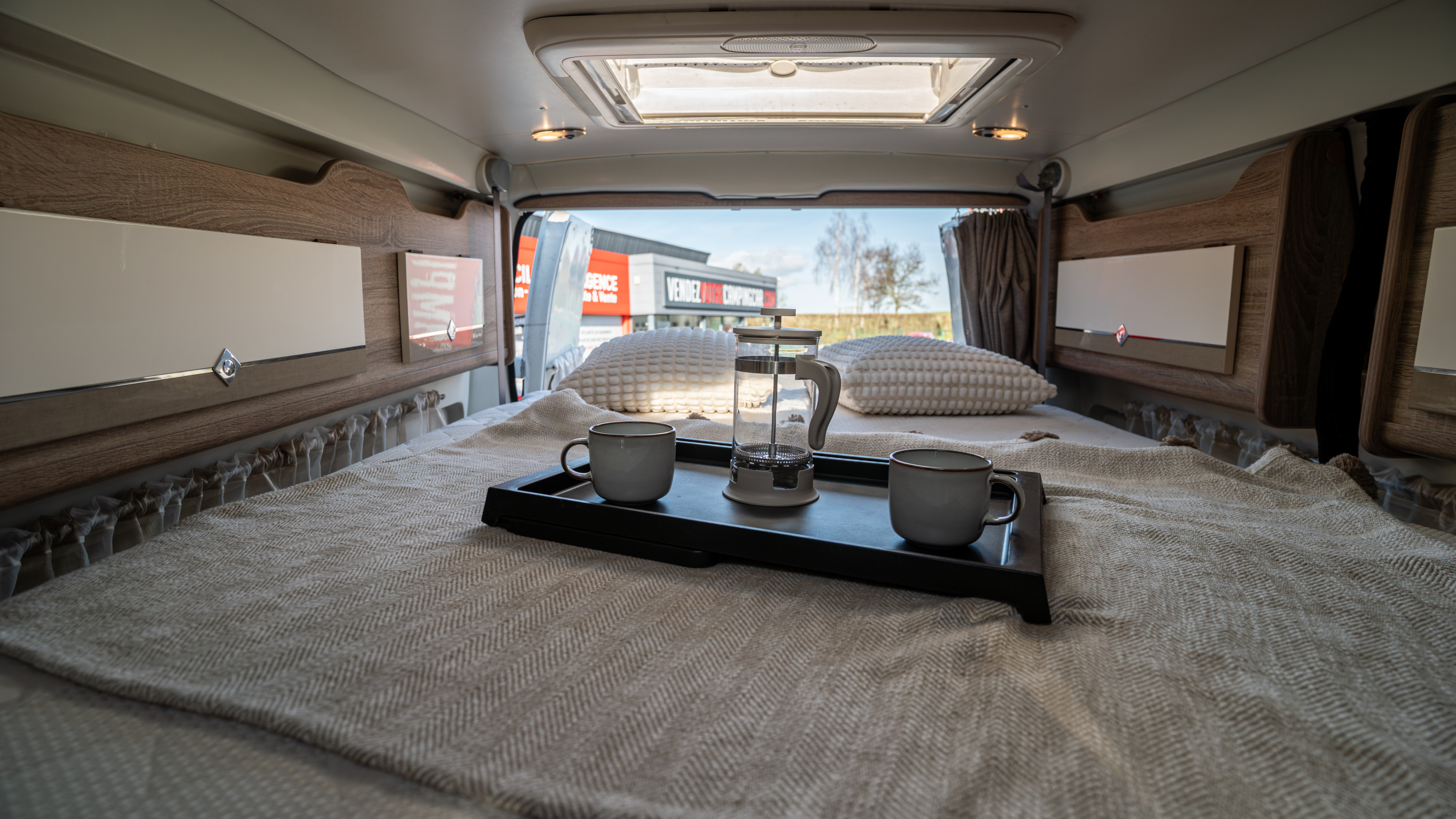 Cozy RV rental interior with a comfy bed, coffee setup, and outdoor views from the open back. Ideal for travel.. Font vendôme Plaisance D 2015