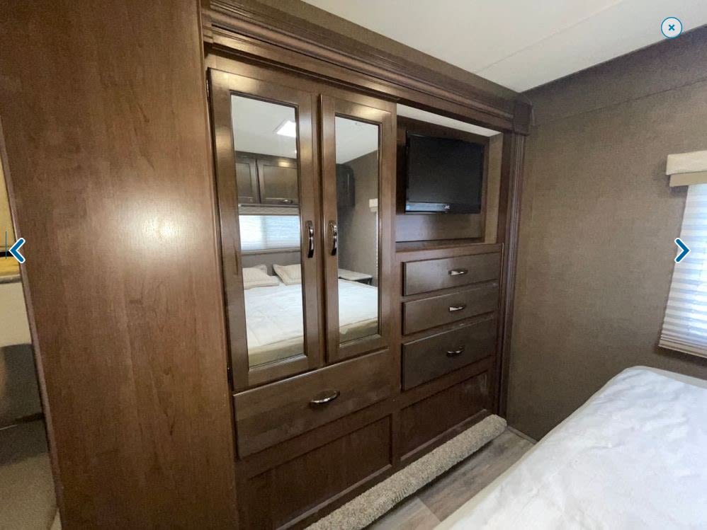 RV rental bedroom showcasing a wooden wardrobe with mirrored doors, built-in TV, and drawers for storage.. Thor Freedom Elite 2021