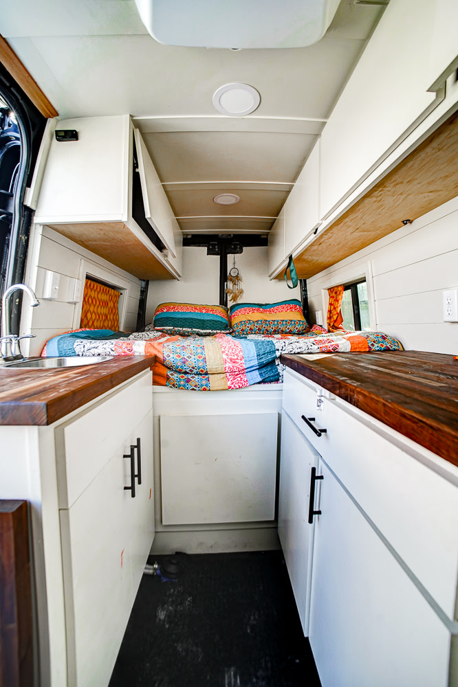Cozy RV rental campervan interior with a colorful bed, kitchenette, and ample overhead storage for travel comfort.. Mercedes-Benz Sprinter 2019