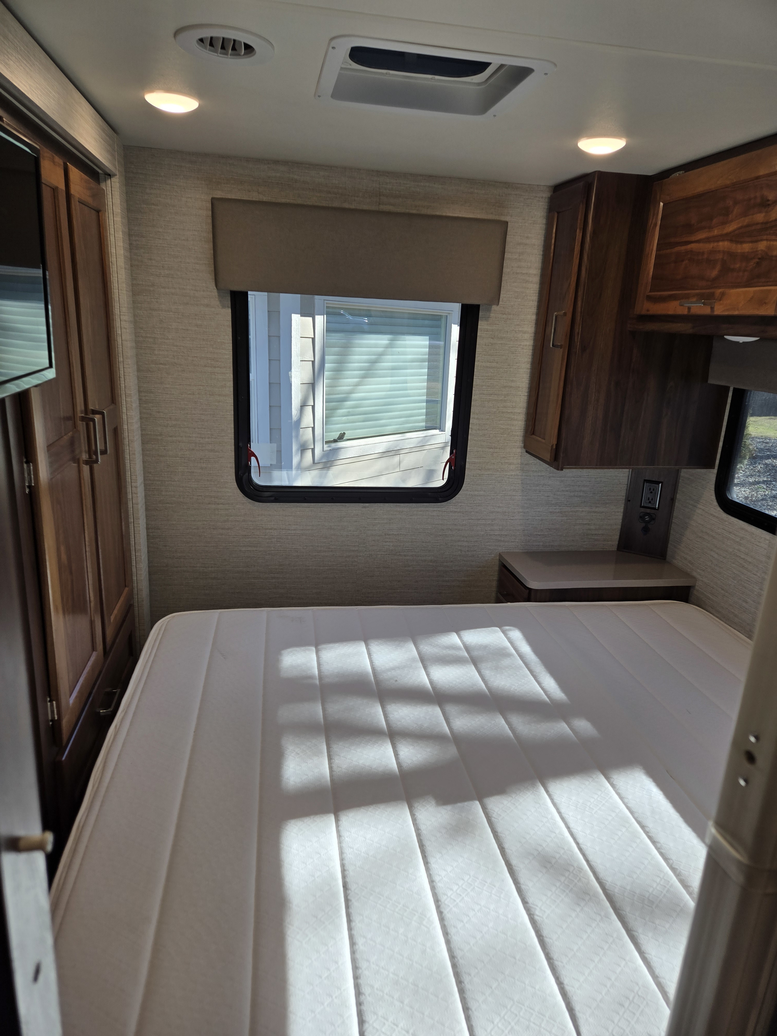 Inviting RV rental bedroom with a bright white mattress, wood storage, window with blinds, and ceiling vents.. Winnebago Minnie Winnie 2020
