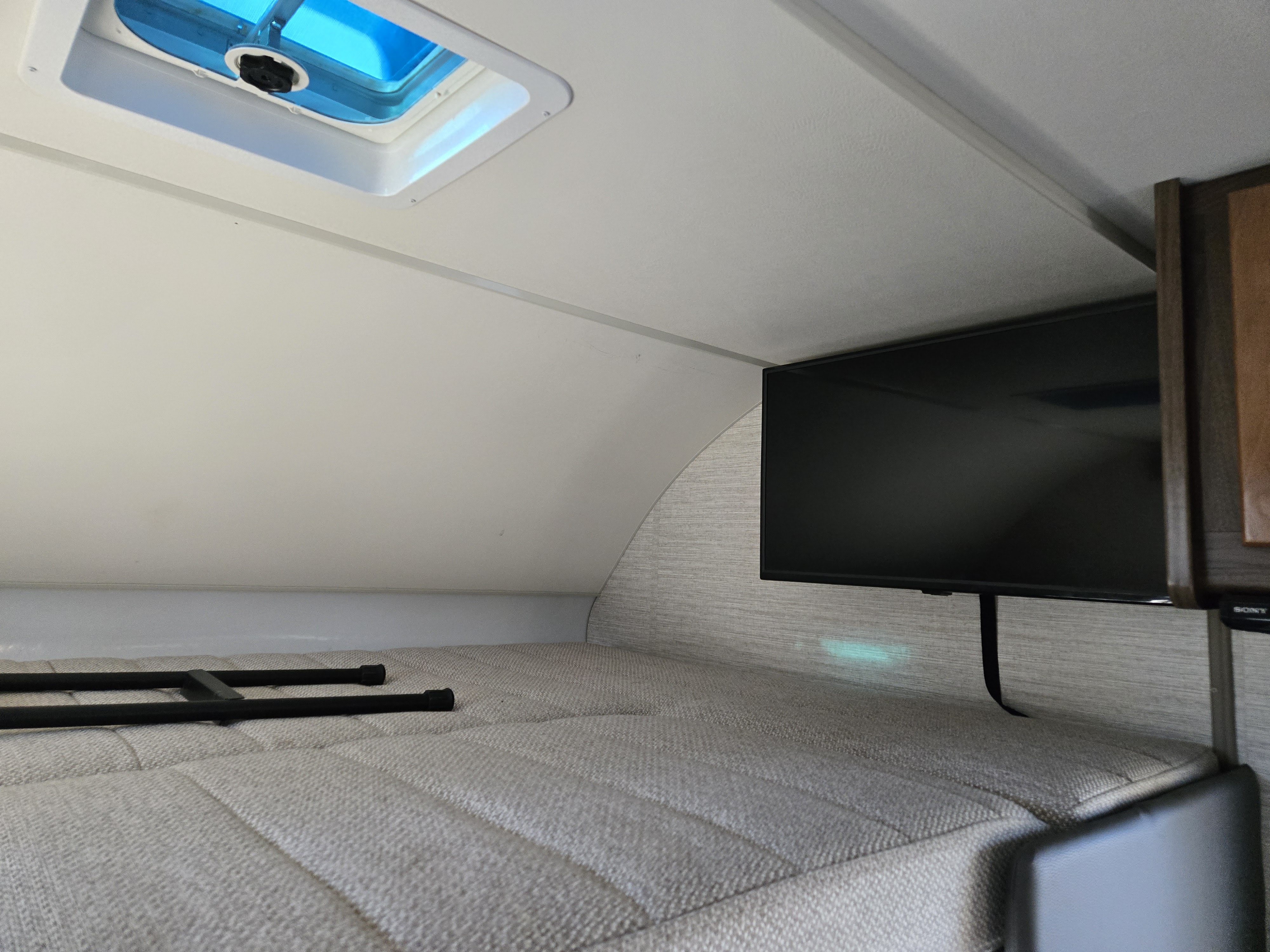 Inside an RV rental: overhead bunk bed with a blue skylight, flat-screen TV, and ladder on soft cushions.. Winnebago Minnie Winnie 2020