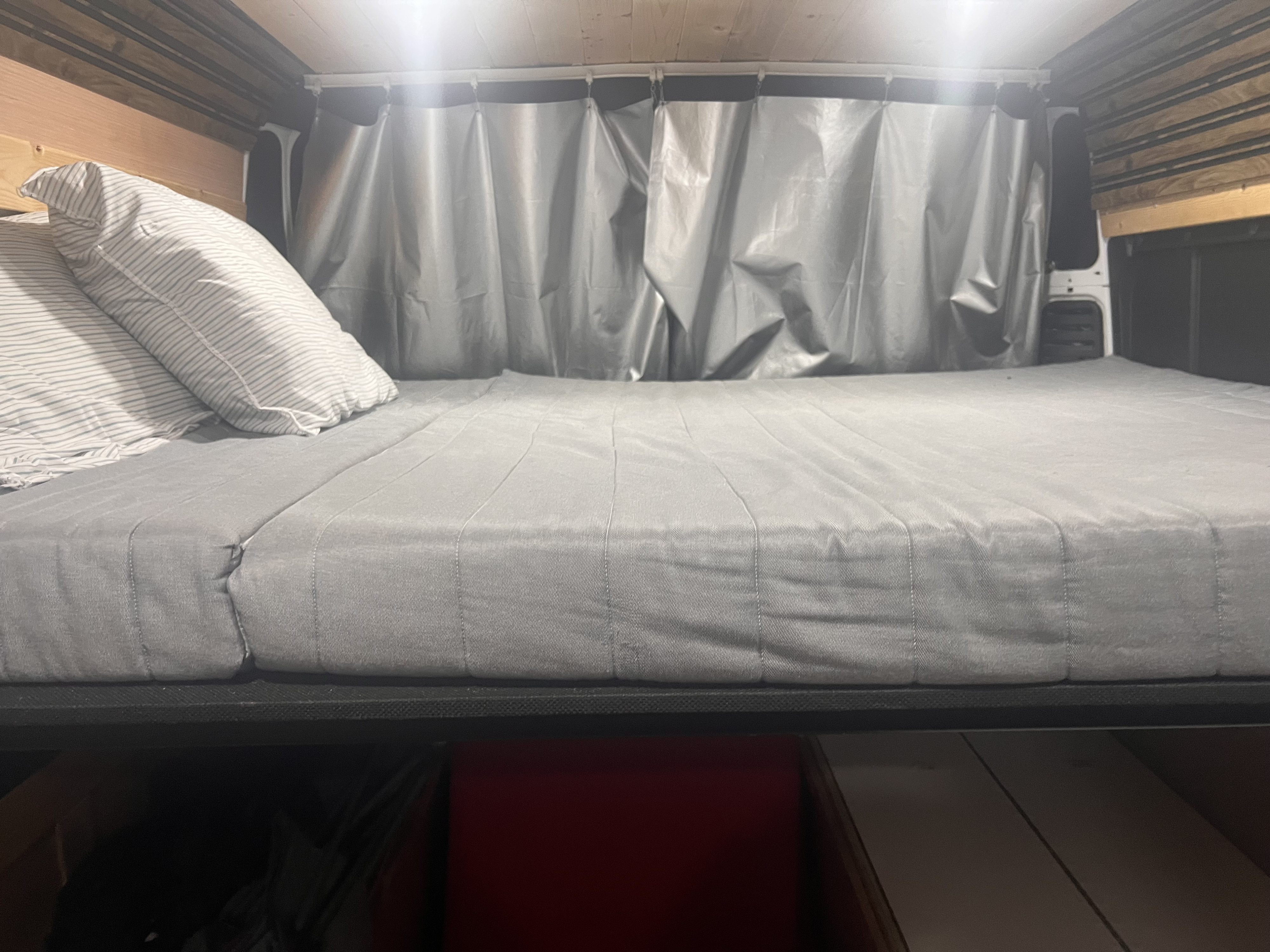 RV rental: Cozy sleeping area with gray mattress, striped pillows, and privacy curtains in a functional campervan interior.. Ram Promaster 2019