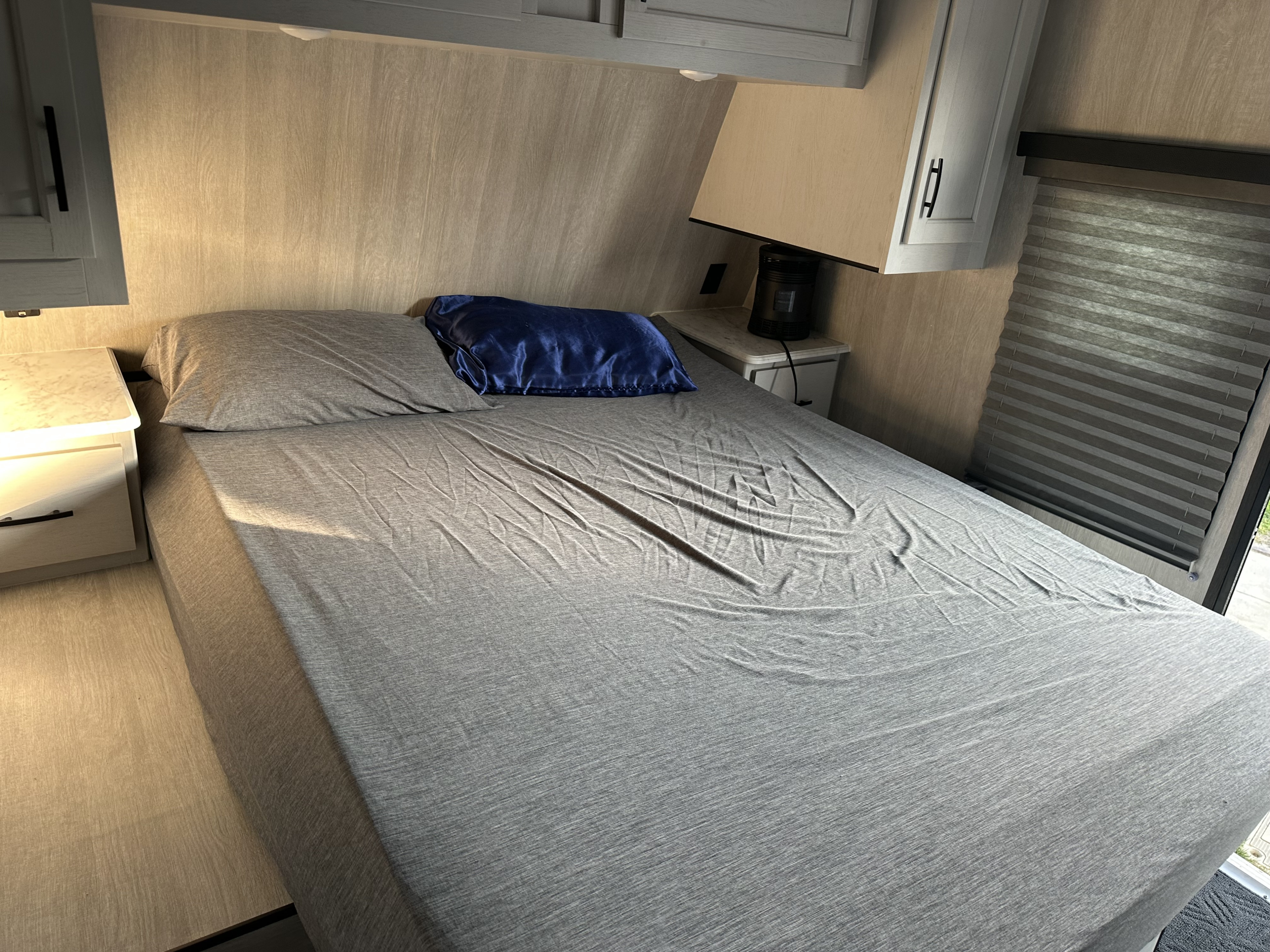 RV rental bedroom: a neat grey bed with a blue pillow, nightstands, overhead cabinets, and a window blind.. Genesis Supreme Seabreeze 27RLS 2024
