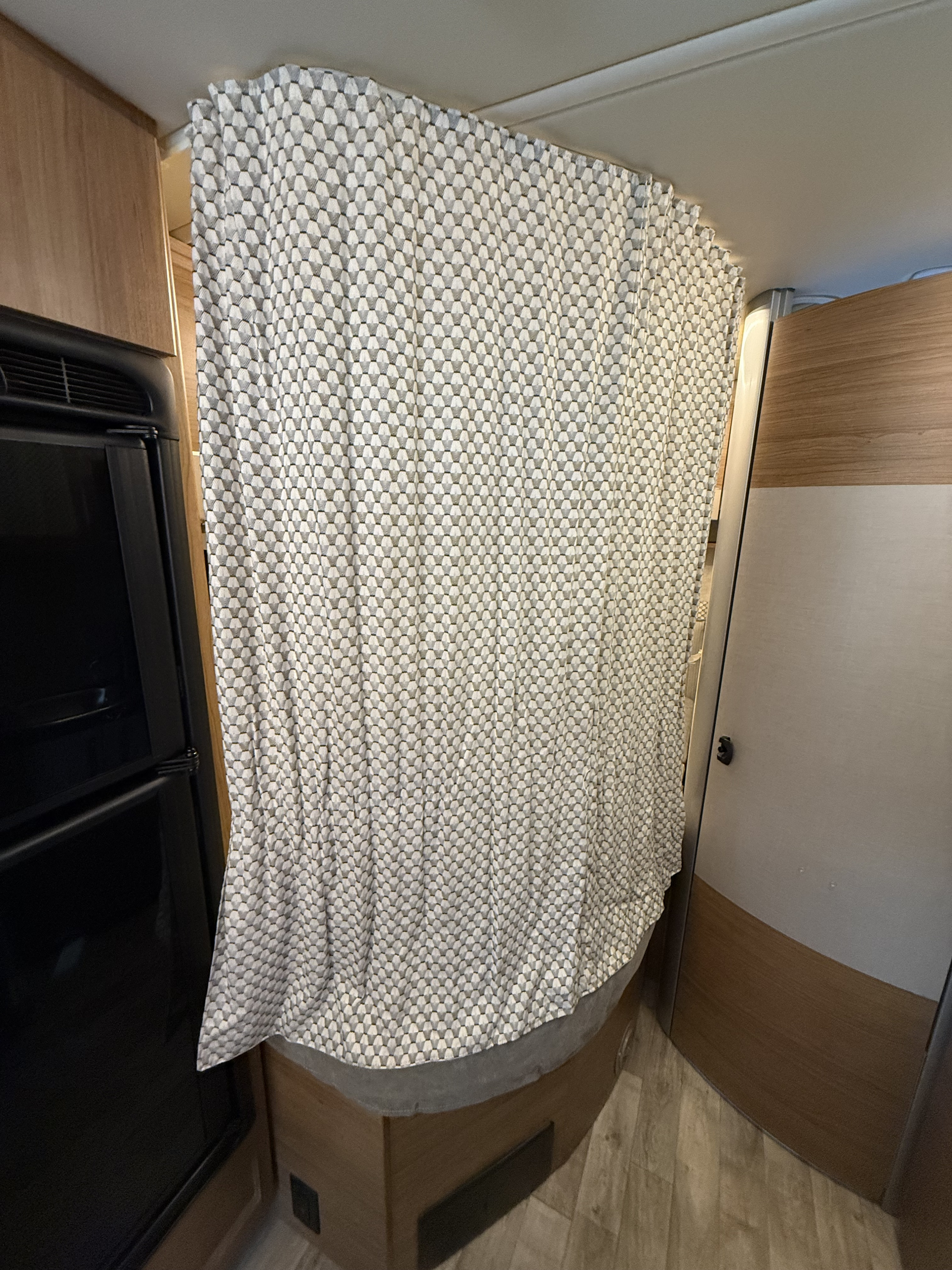 Privacy curtain inside an RV rental, sectioning off a sleeping area or bathroom next to a refrigerator and wooden walls.. Winnebago View 2019