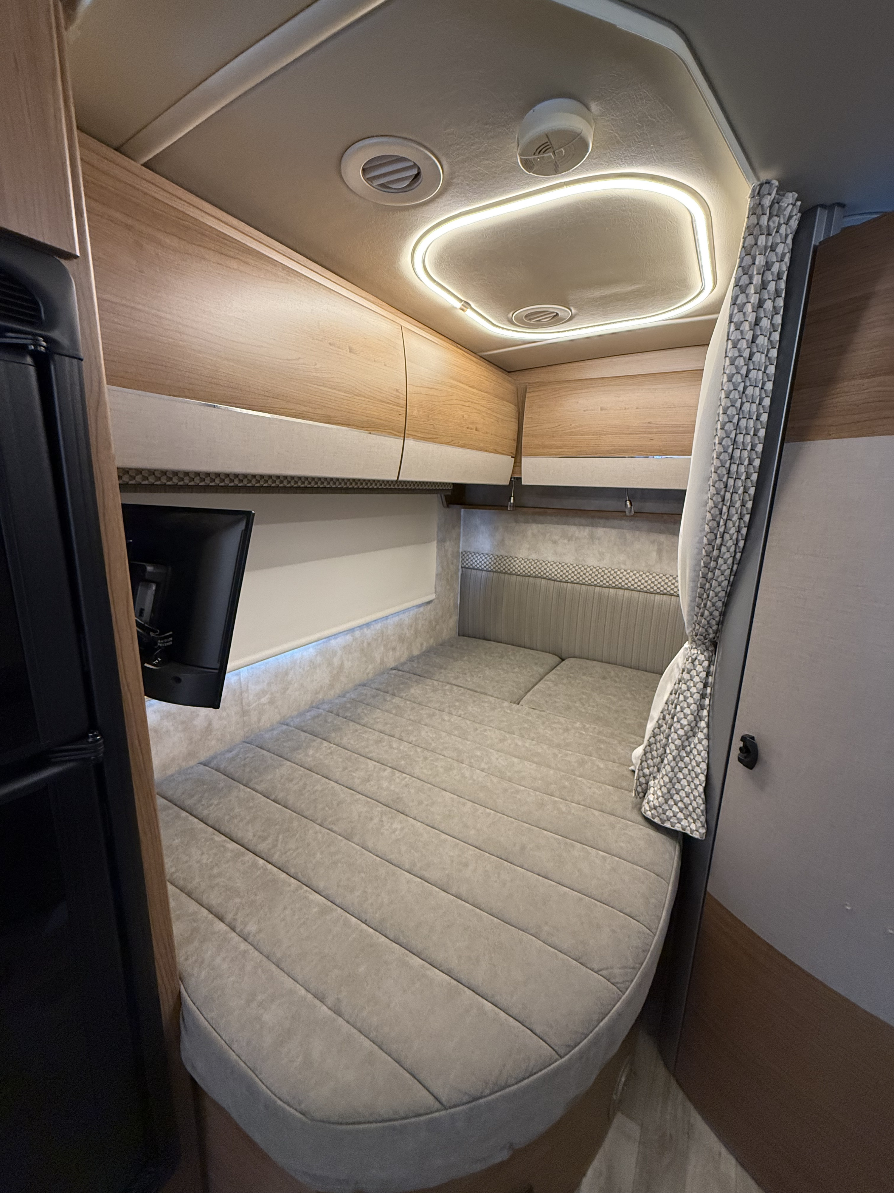 Explore this RV rental's modern interior: a cozy grey bed, light wood cabinets, wall-mounted TV, and bright LED lighting.. Winnebago View 2019