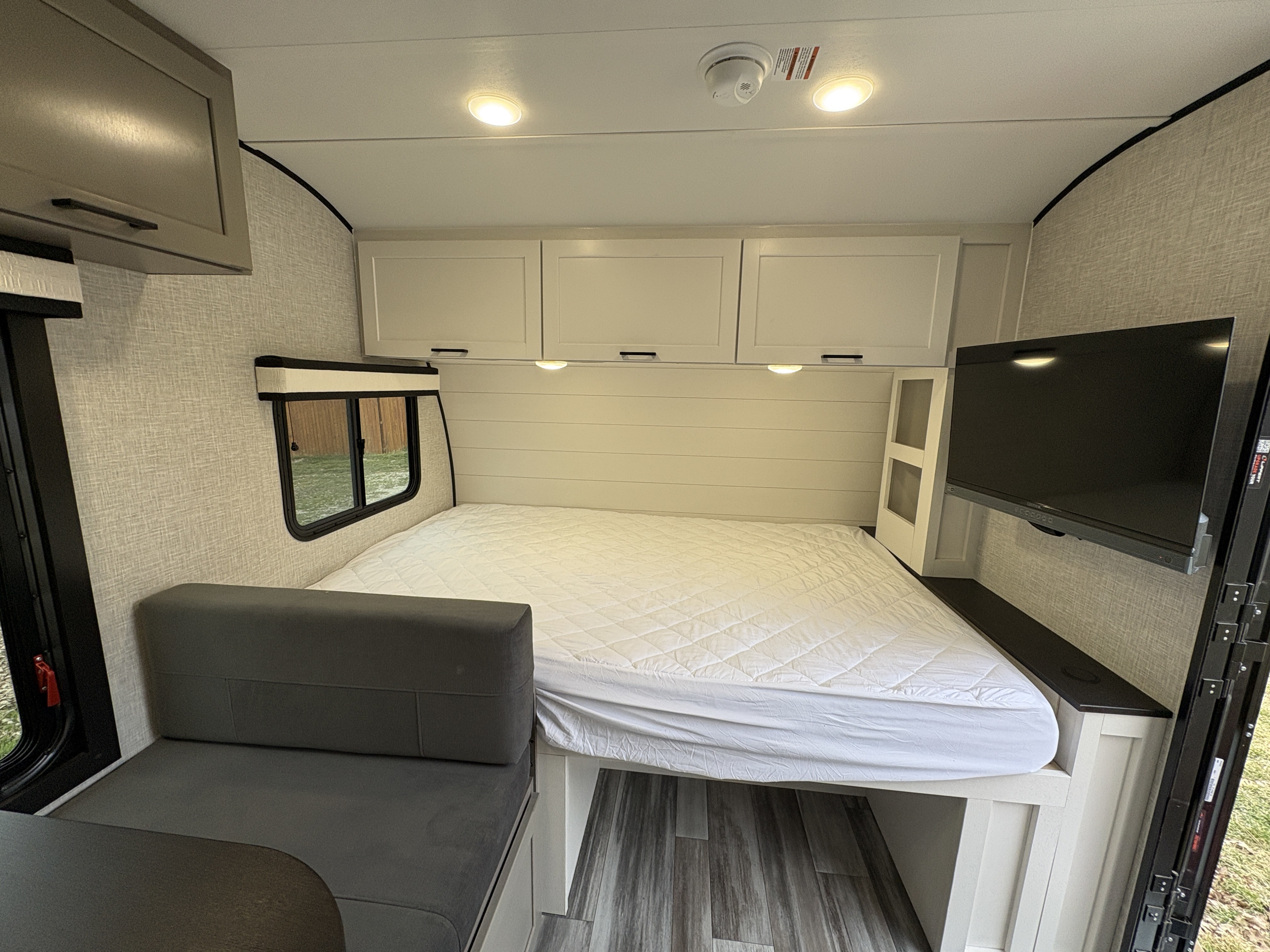 This RV rental interior features a comfortable bed, cozy dinette, overhead cabinets, and a wall-mounted TV for relaxation.. Jayco Jay Feather Micro 2025