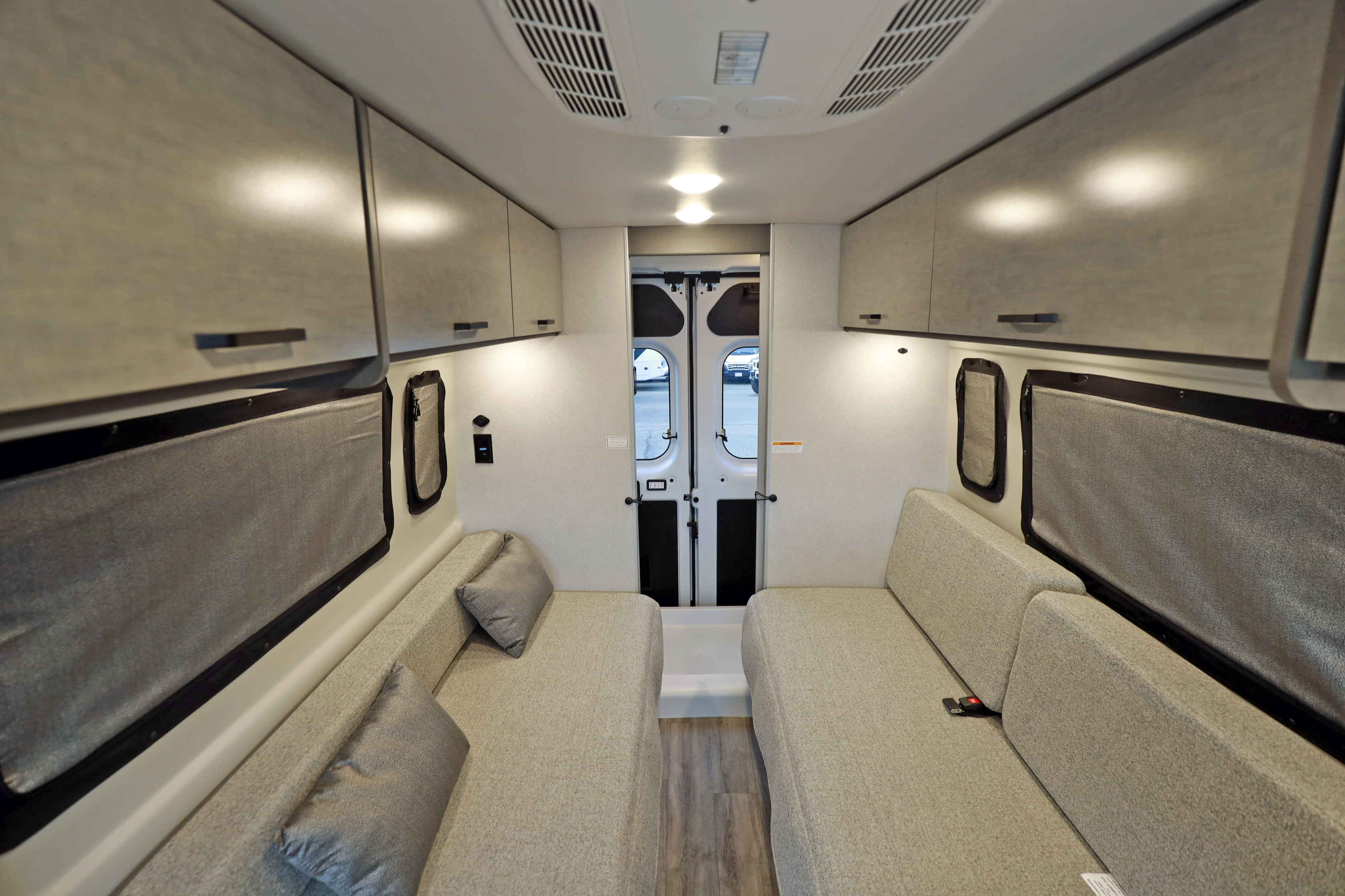 Spacious camper van interior for RV rental, featuring cozy benches, overhead cabinets, and modern design, looking towards the rear doors.. Thor Motor Coach twist 2022