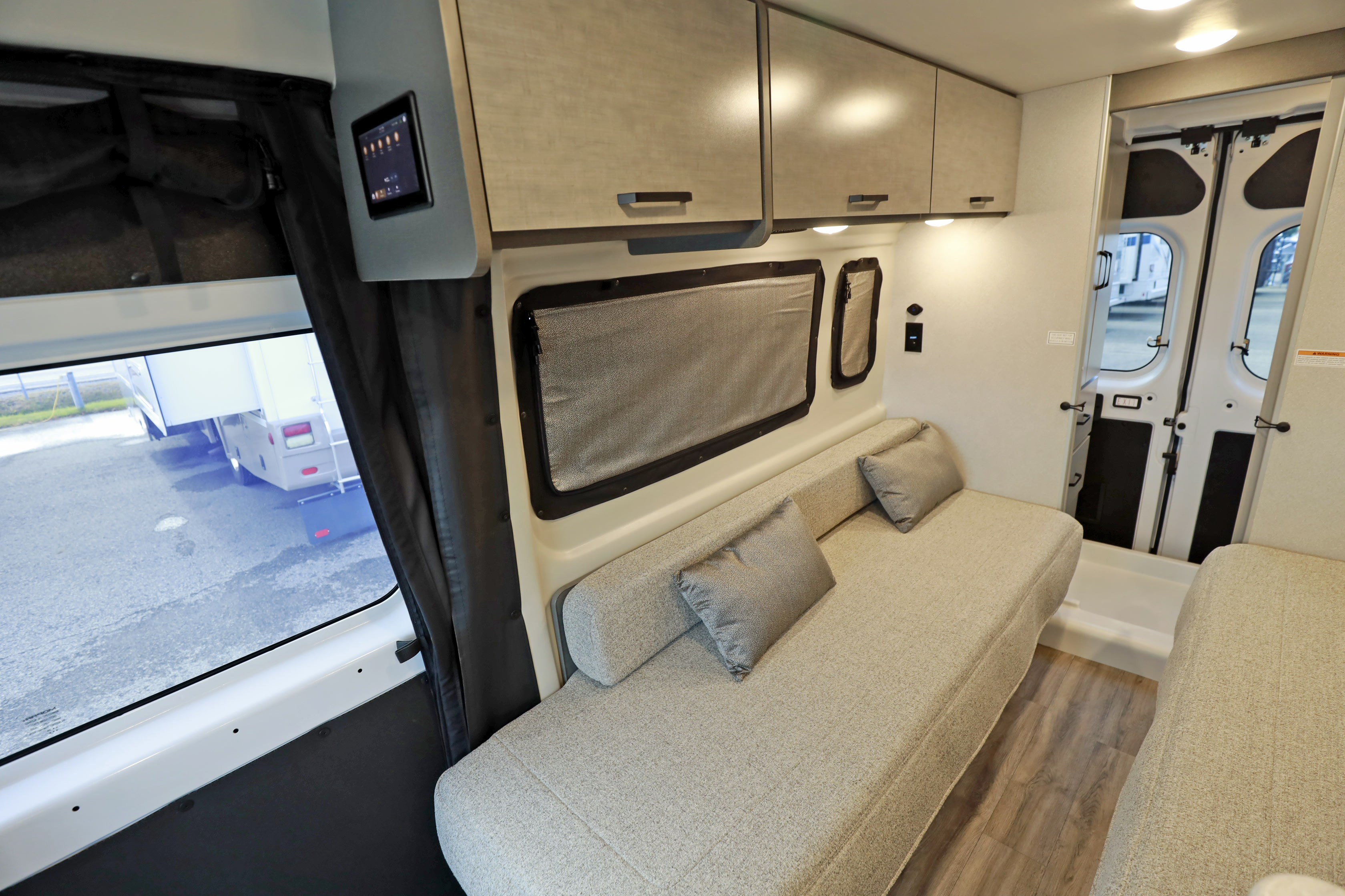 Cozy rv rental interior features a long bench seat with cushions, overhead cabinets, and a digital control panel for comfortable travel.. Thor Motor Coach twist 2022
