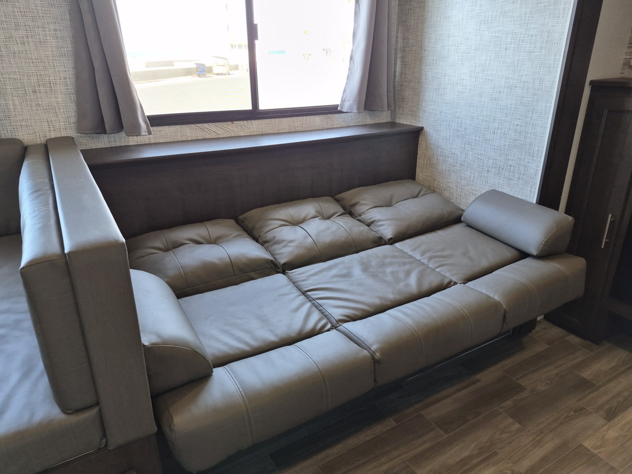 Inside your RV rental: a versatile gray sofa bed extended for lounging or sleeping, next to a bright window.. Forest River Salem Cruise Lite 2020