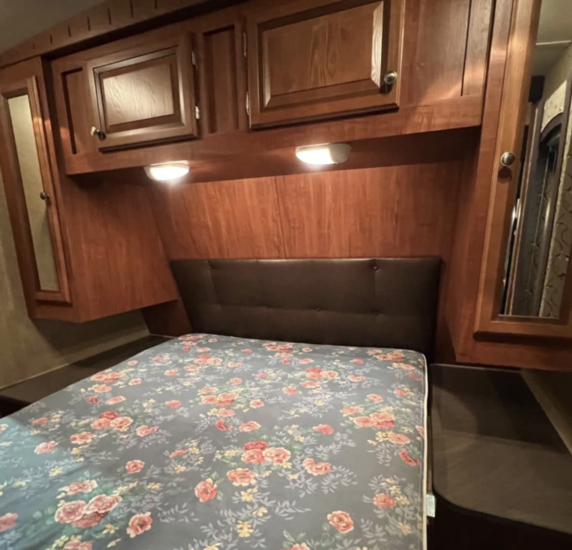 Interior of an RV rental bedroom featuring a bed with floral cover, headboard, wood cabinetry, and bedside mirrors.. Jayco Eagle 2020