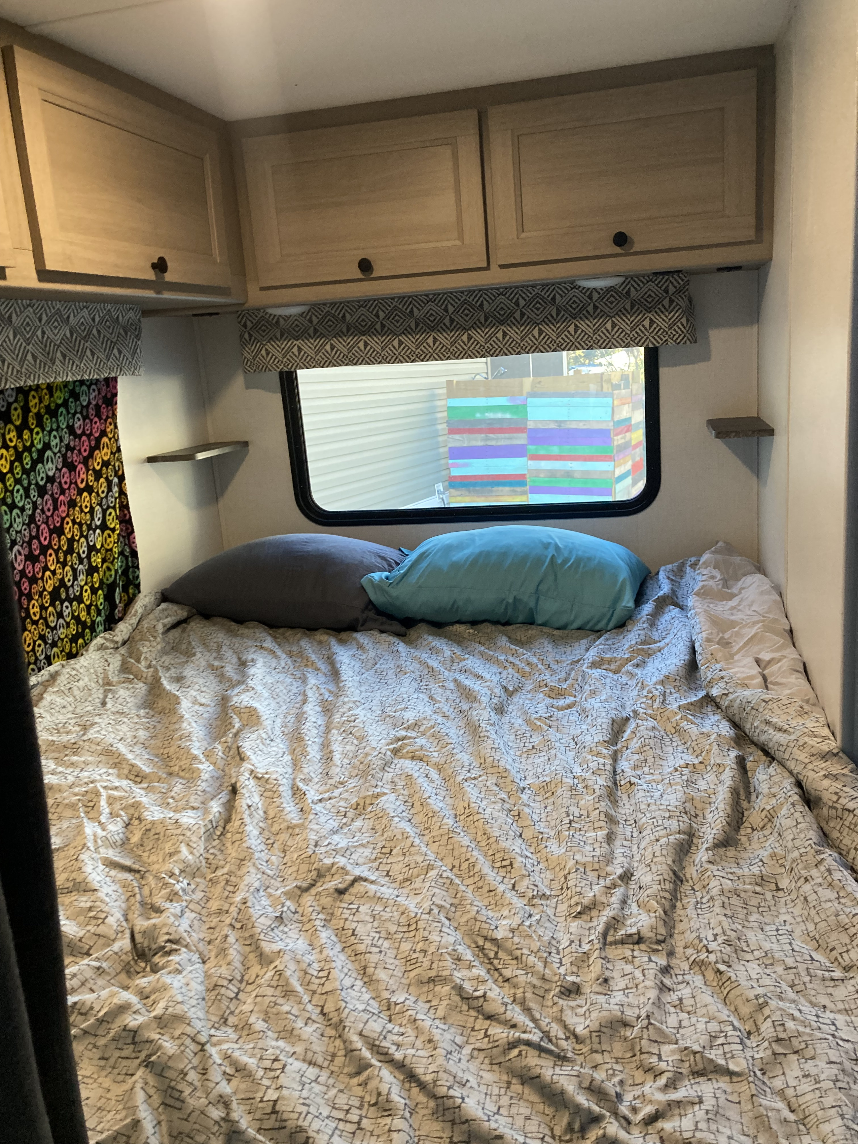 An RV rental bedroom features a bed with grey and blue pillows, patterned bedding, overhead cabinets, and a window.. Forester LE 2024