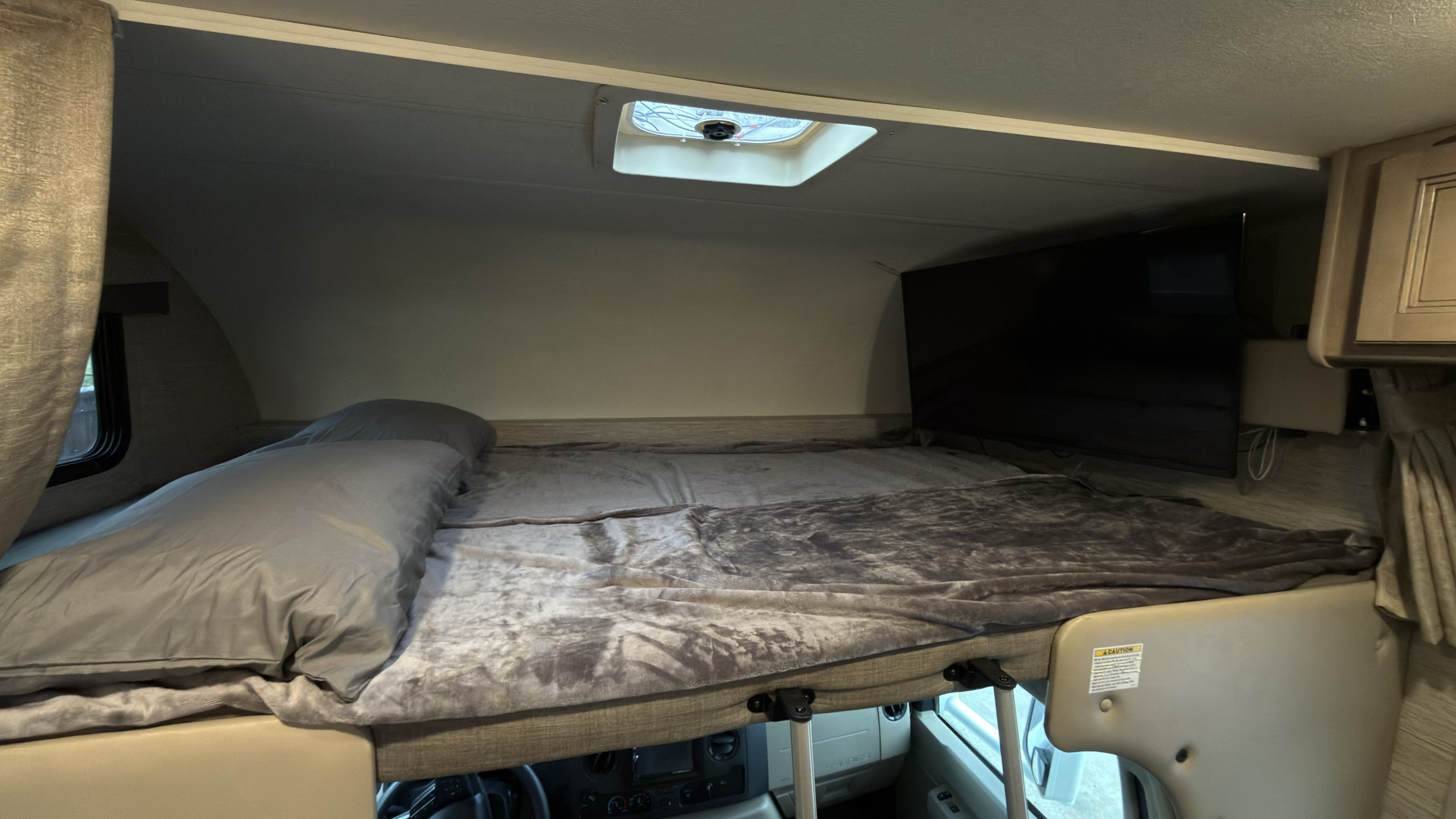 RV rental: cozy over-cab bunk bed with grey bedding & TV, providing a comfortable sleeping area in the RV interior.. Thor Four Winds 2022