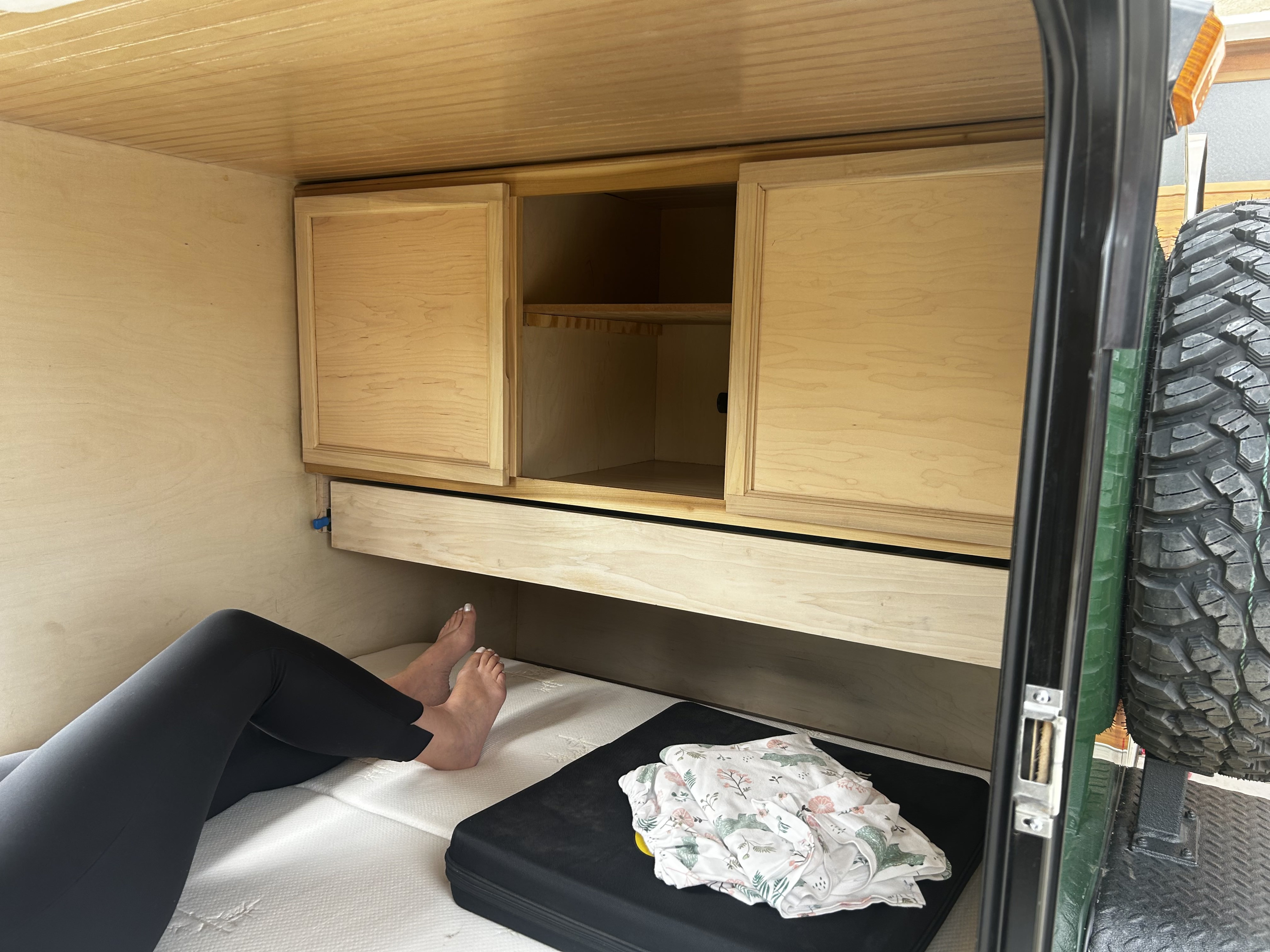 Cozy rv rental camper interior: person relaxing on a bed next to wooden cabinetry, shelves, and a storage drawer.. OK Schooners CS 10 2022