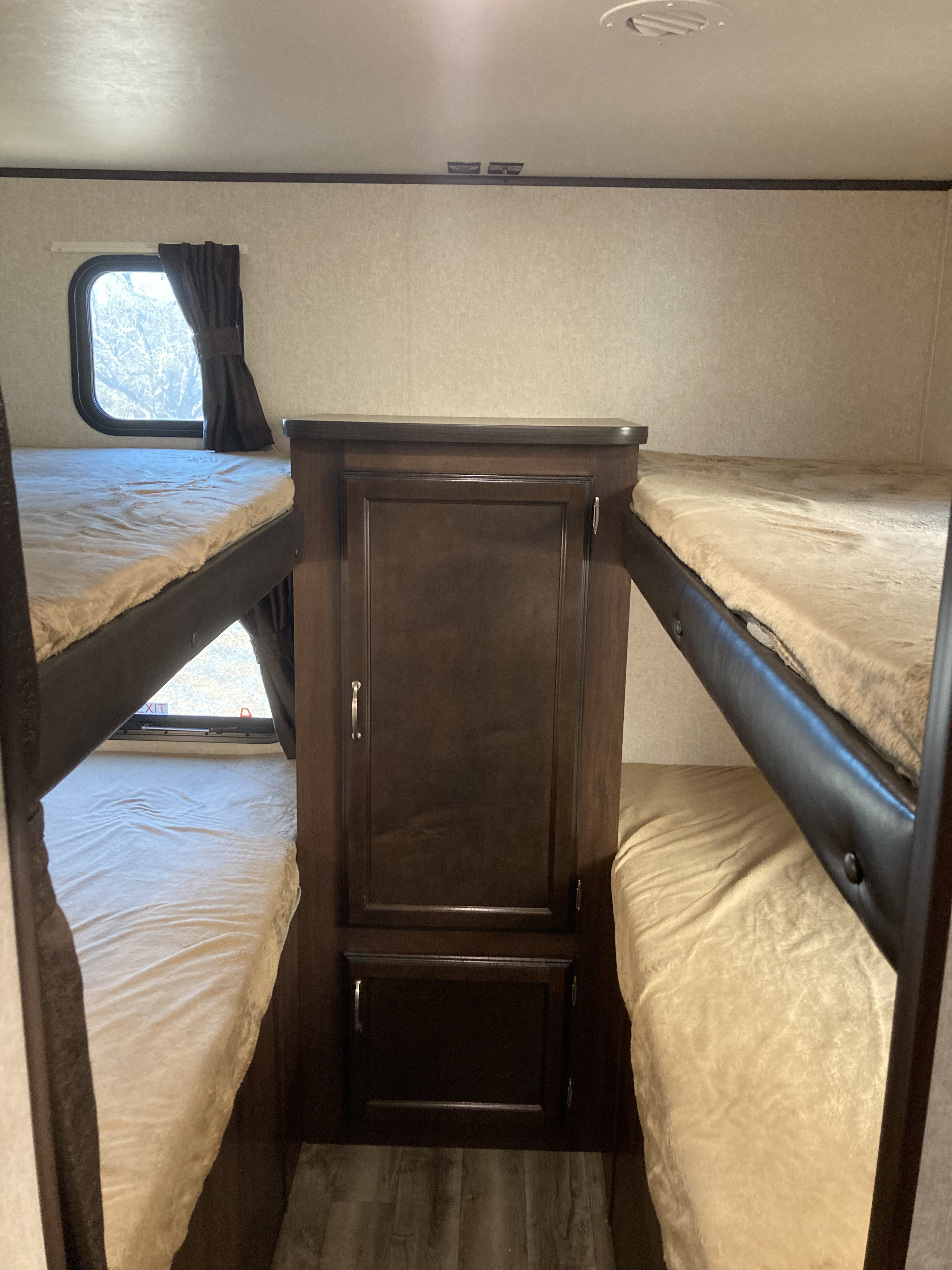 Cozy bunk beds in an RV rental interior, separated by a dark wood cabinet, with a window on the left side.. Jayco Jay Flight SLX 2018