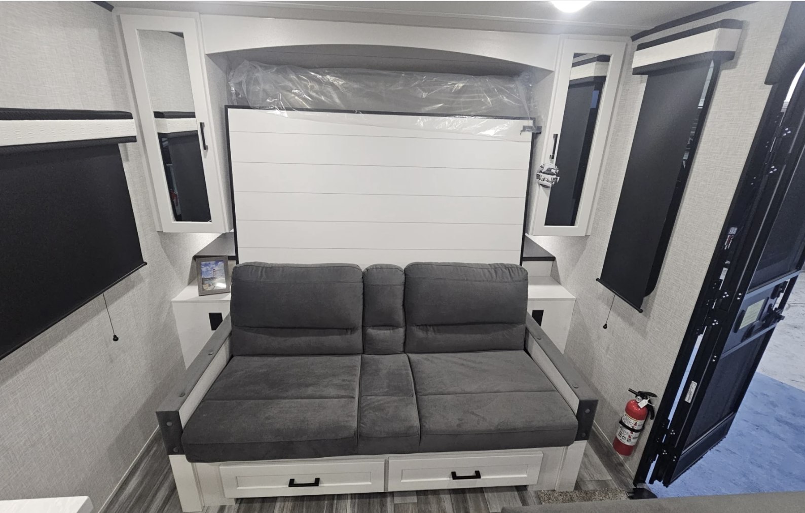 RV rental: Modern interior featuring a gray sofa, storage drawers, and a fold-down murphy bed, with black blinds and a fire extinguisher.. Jayco JayFeather AIr 2025
