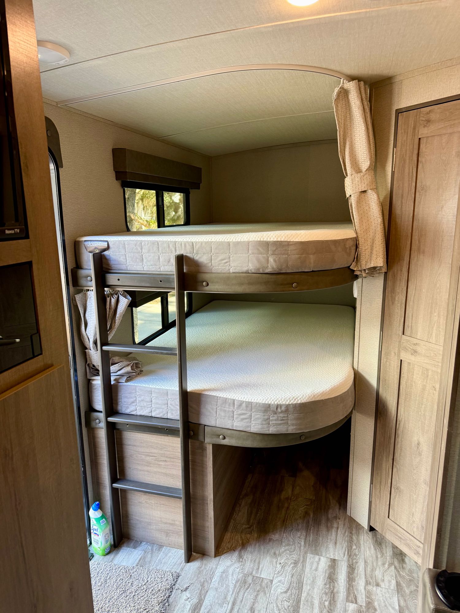 Compact bunk beds in an RV rental, offering a cozy sleeping area with mattresses, windows, and curtains. Ideal for family trips.. Grand Design Imagine 2022