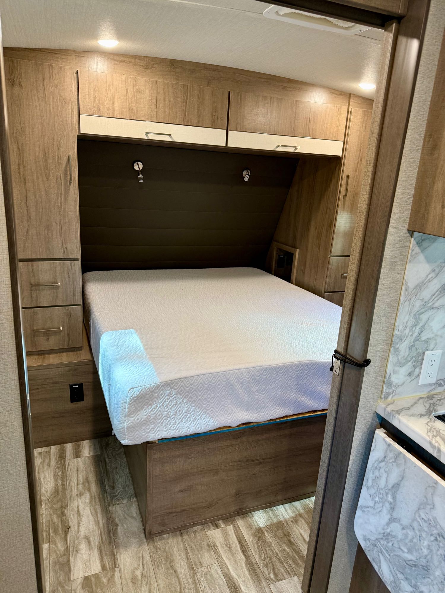 This RV rental offers a cozy bedroom with a queen bed, overhead and side storage, and modern wood finishes.. Grand Design Imagine 2022