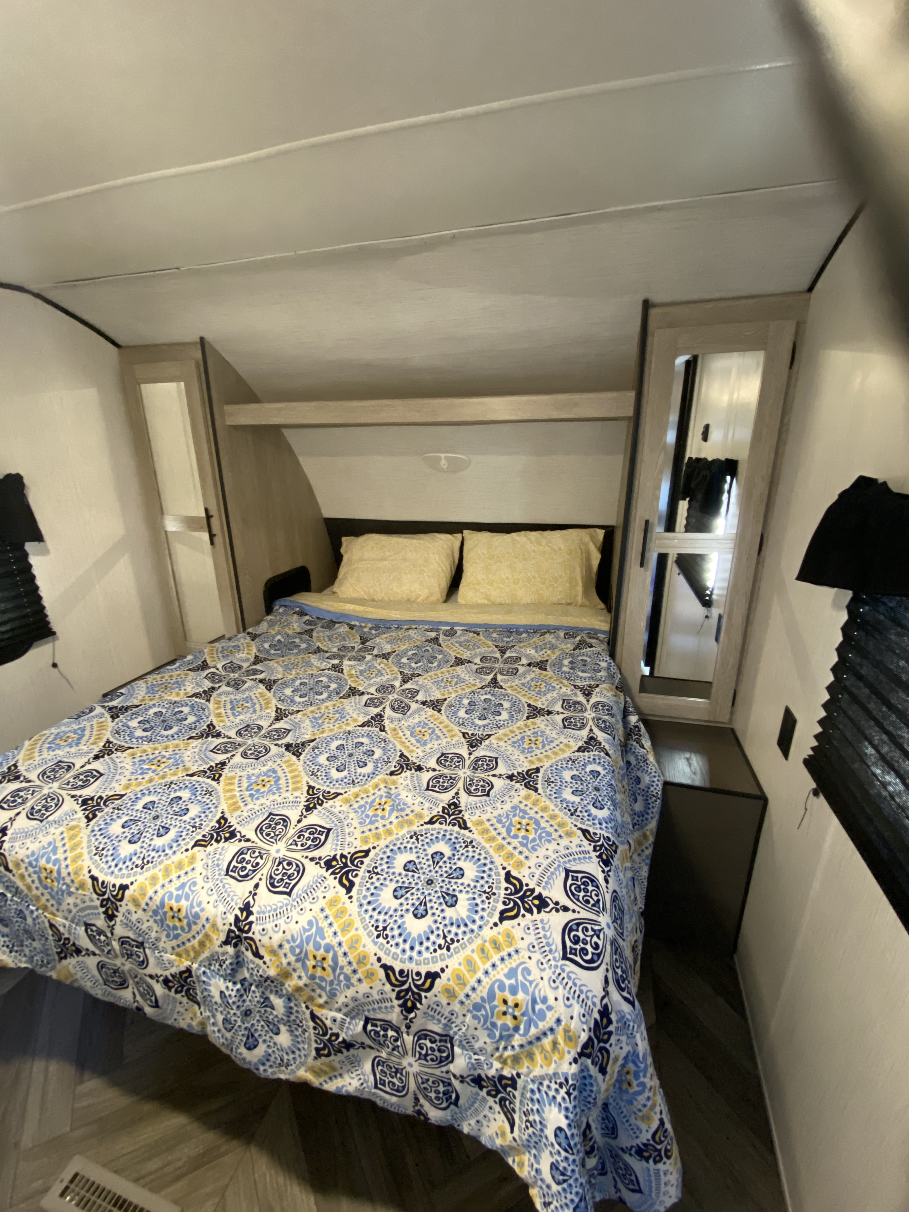 Inside a comfortable **rv rental** bedroom, featuring a vibrant blue, yellow, and white patterned bedspread and convenient bedside storage.. Keystone RV Cougar 2022