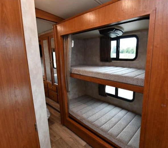 Inside an RV rental: cozy bunk beds with windows, an AC unit, and nearby storage. Ideal for family adventures.. Winnebago Vista 2019