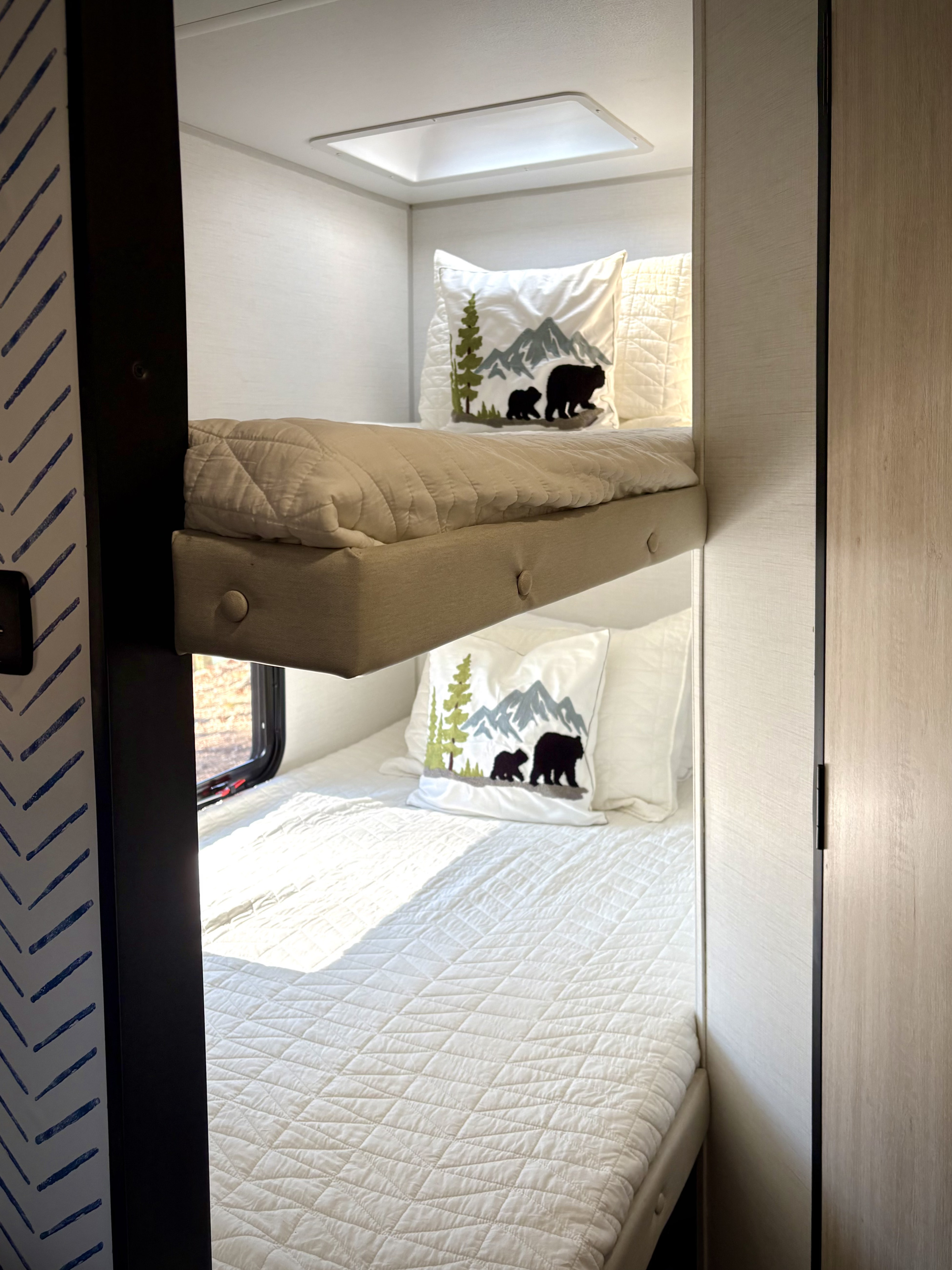 Bunk beds in an RV rental, featuring bear-themed pillows and white quilted bedding, illuminated by natural light.. Avenger LT 2024