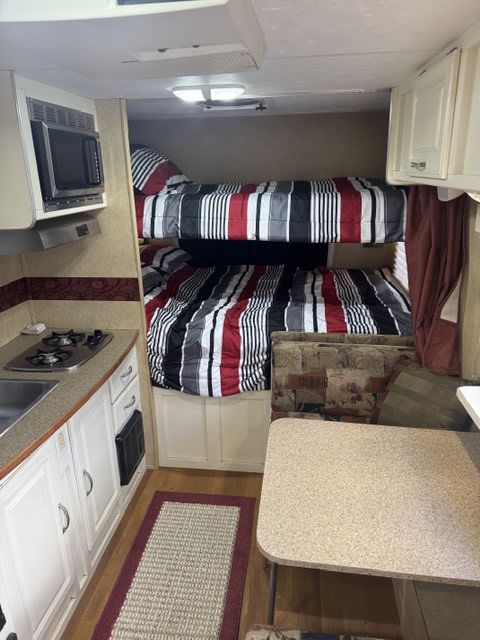 Cozy rv rental interior with bunk beds, a compact kitchen (stove, microwave), and dinette seating for family adventures.. Cruiser RV Fun Finder X 2008